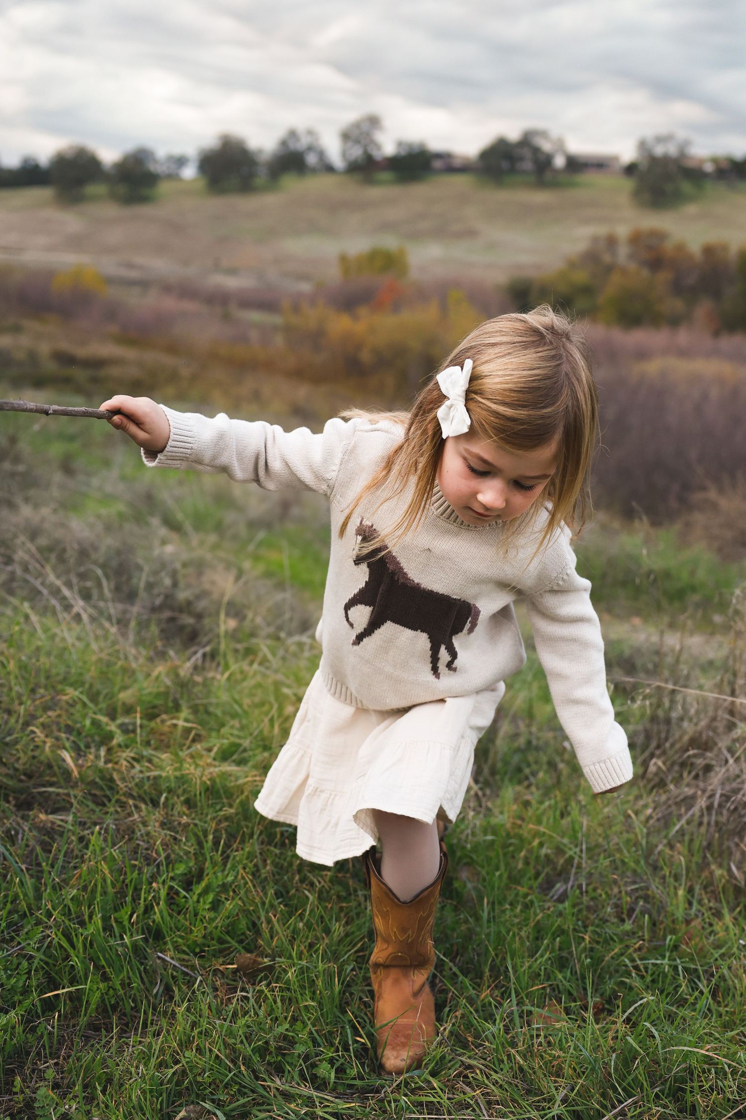 Child in white dress with horse design plays expressively in an autumn field.