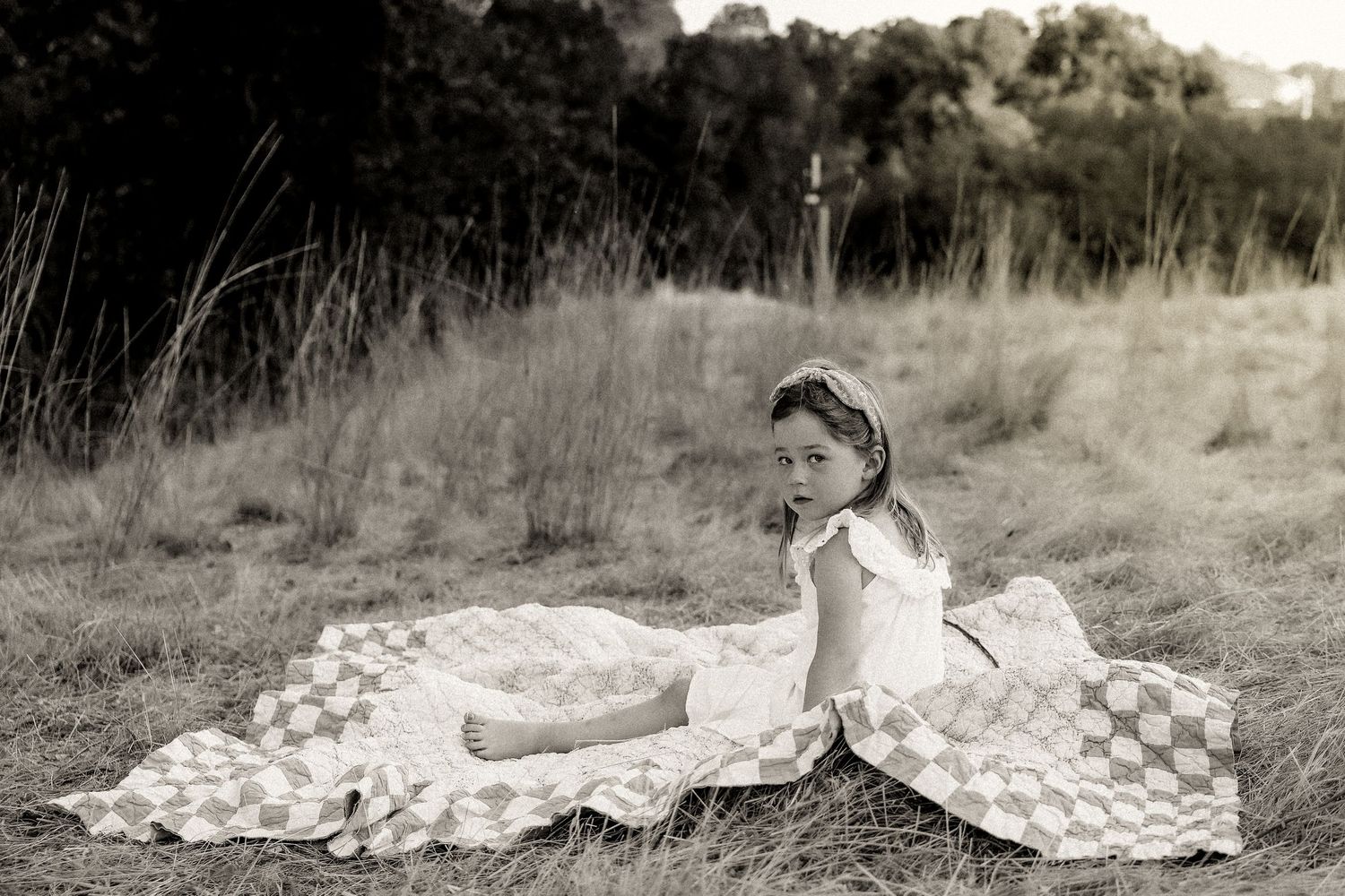 Children relax on checkered blanket in black and white outdoor setting.