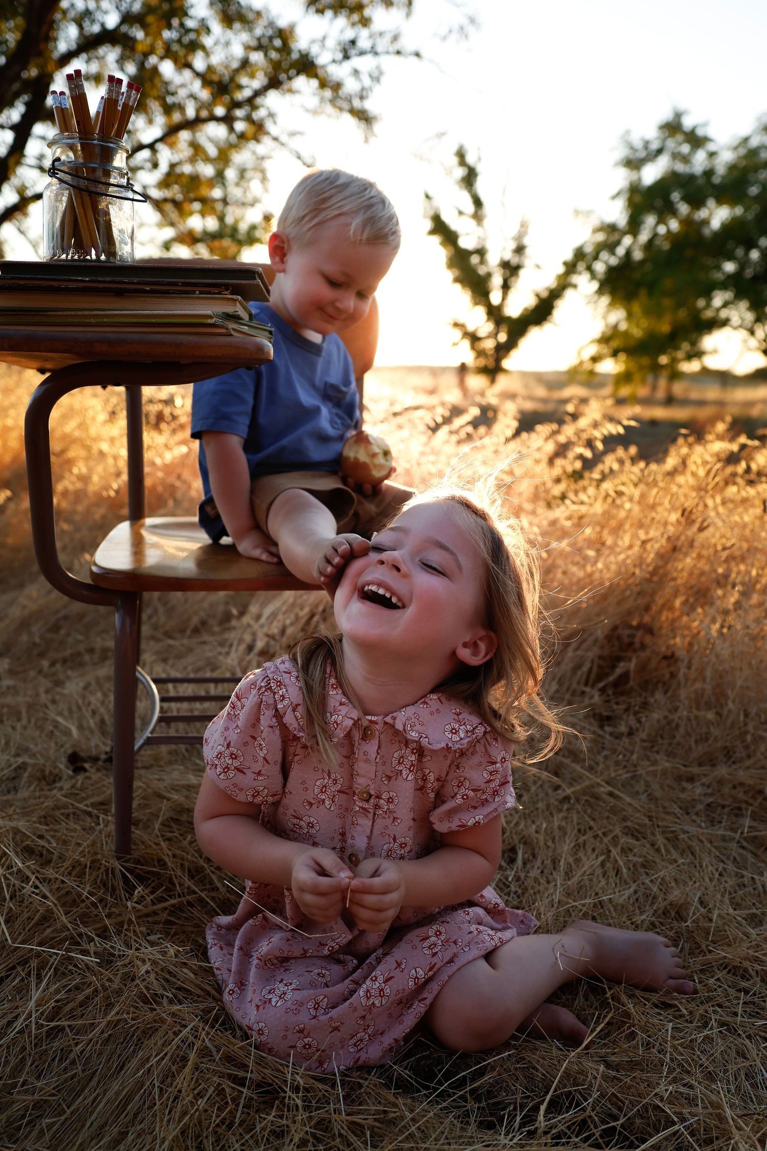 Two children share joyful laughter while playing in a sun-drenched field with vintage furniture.