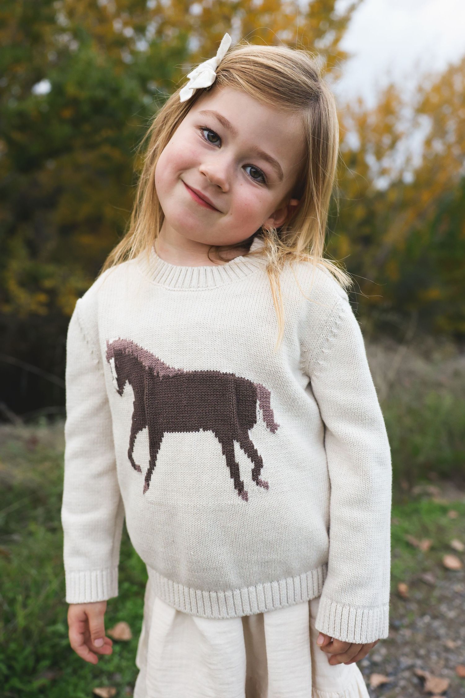 Personality headshot with horse sweater with natural fall backdrop during golden hour.