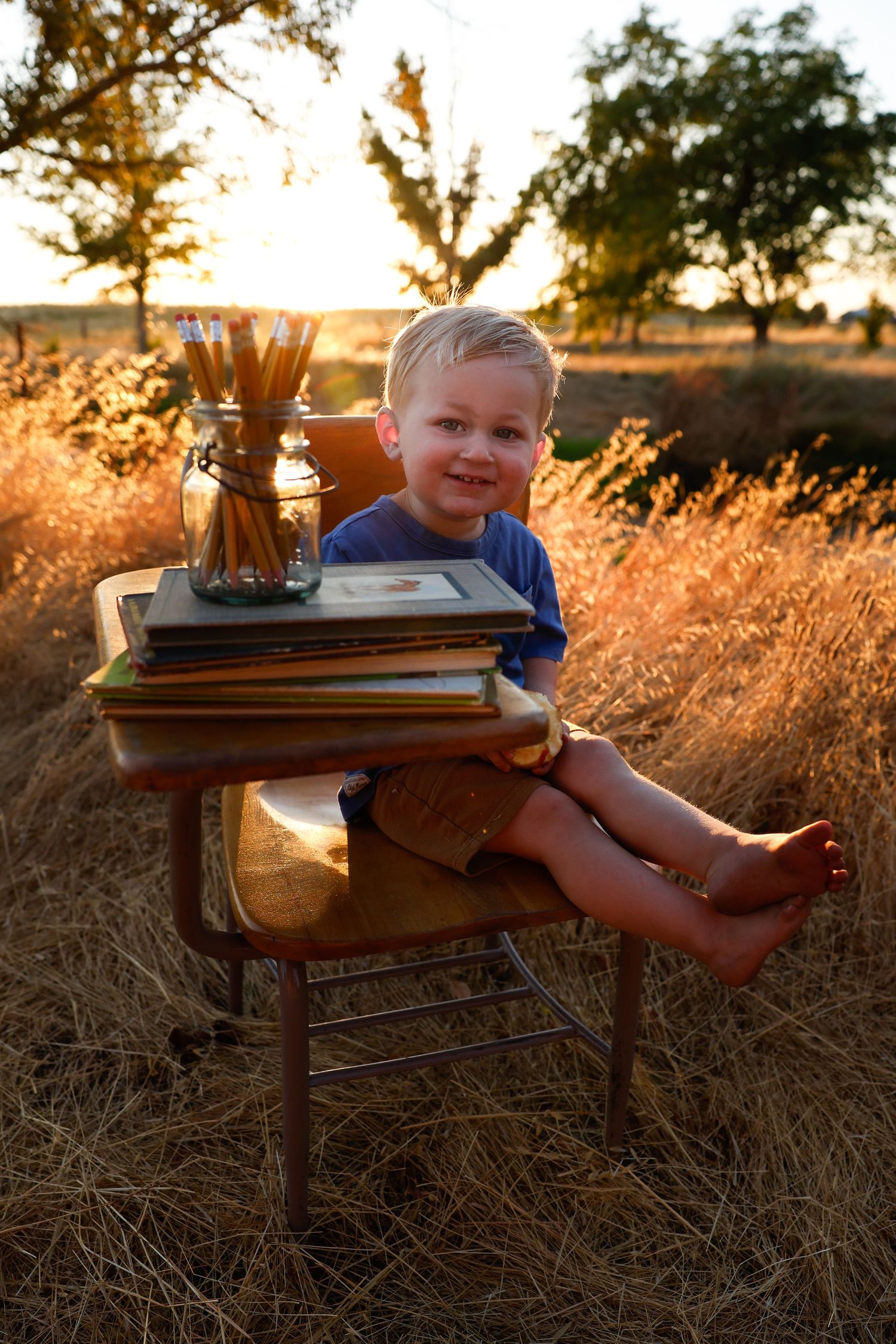 Child relaxes on vintage furniture surrounded by golden grass at sunset.