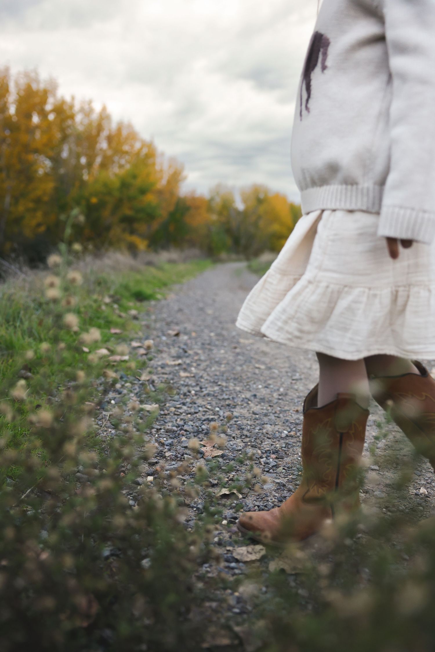 Close-up of boots and dress hem while jumping on gravel path surrounded by autumn vegetation.