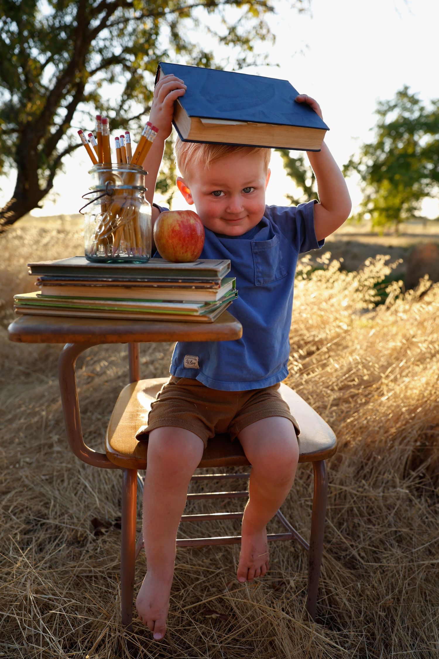 Child in blue shirt sits at antique desk with books and decorative items at sunset.