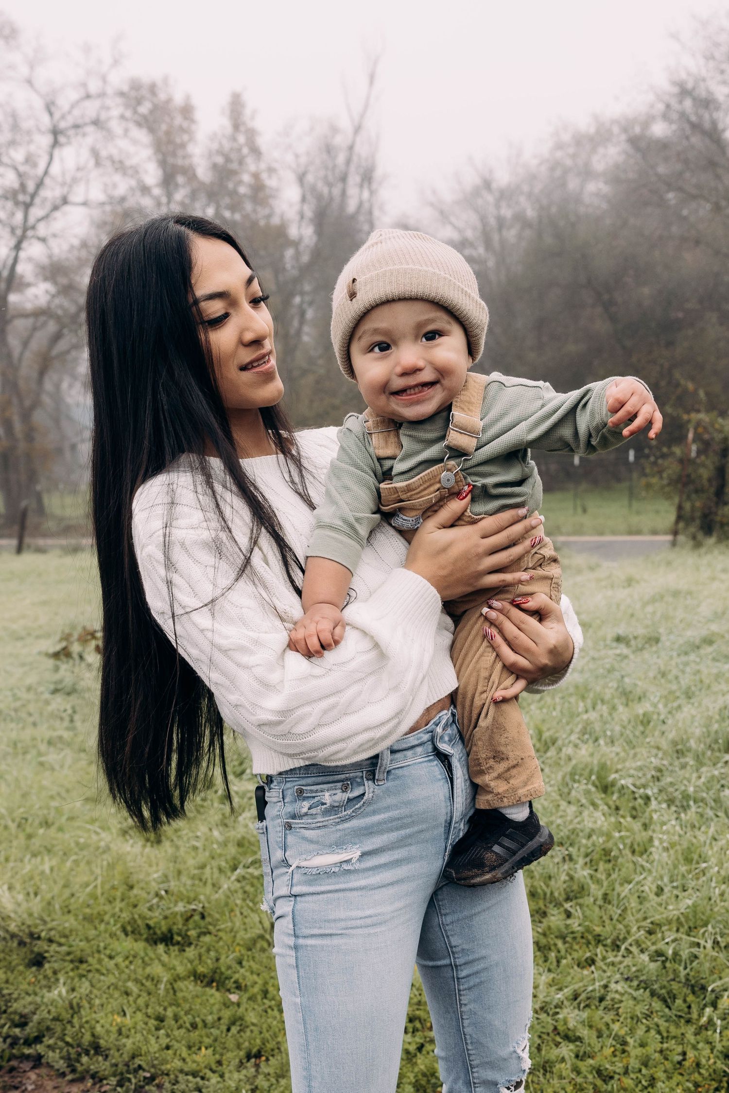 A mother and baby share joyful moments together while playing outdoors in a misty field on an overcast day.