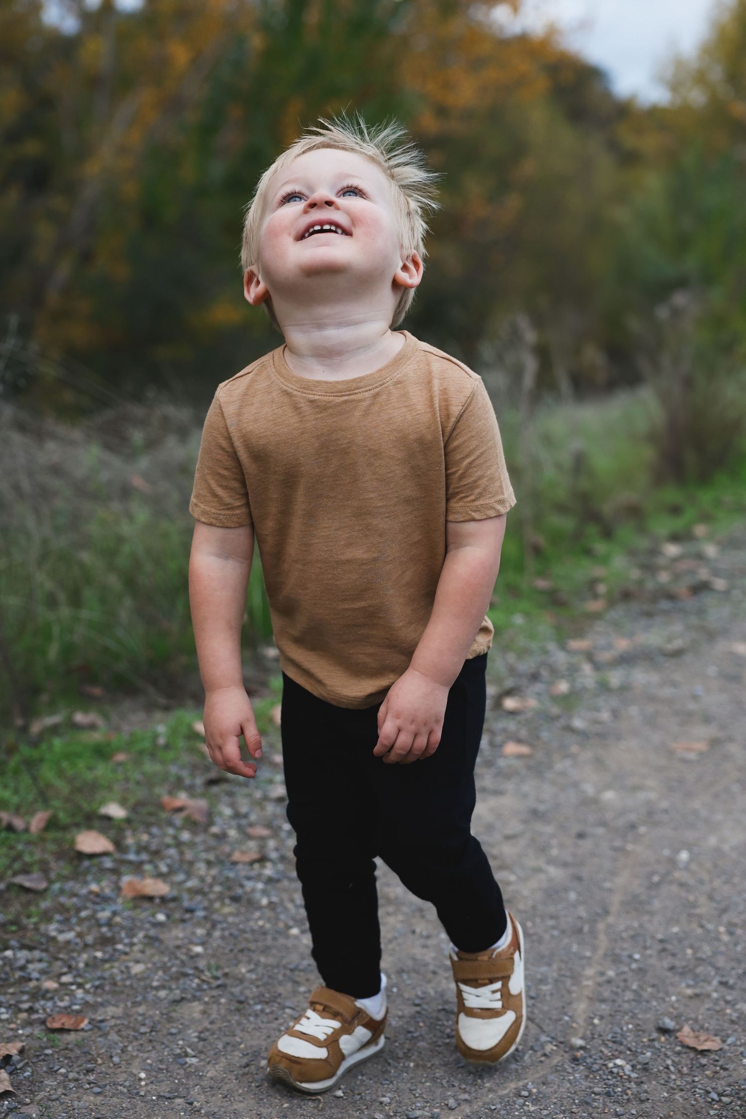 Brown t-shirt and black pants outfit with white sneakers on gravel trail.