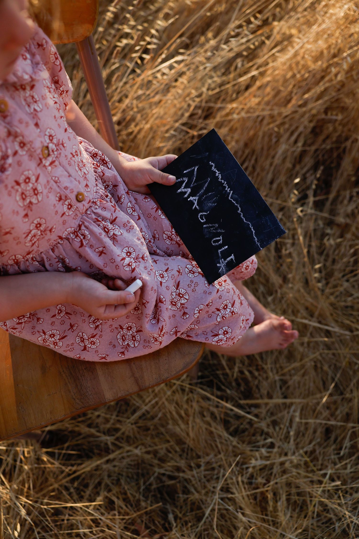 Hands hold a small chalkboard sign against a backdrop of dried golden grass.