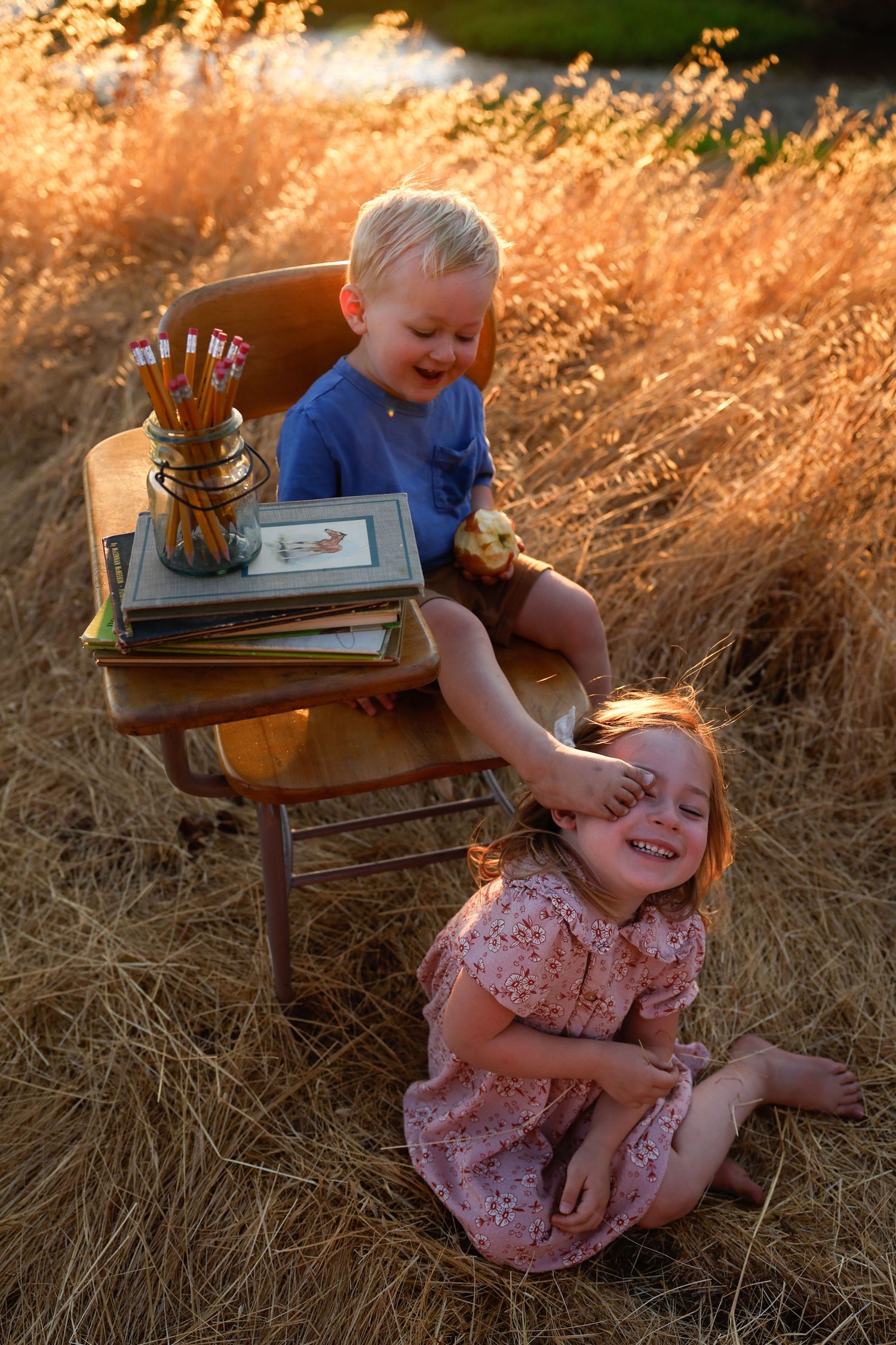 Children playing and laughing together in golden hour light with stacked books on antique furniture.