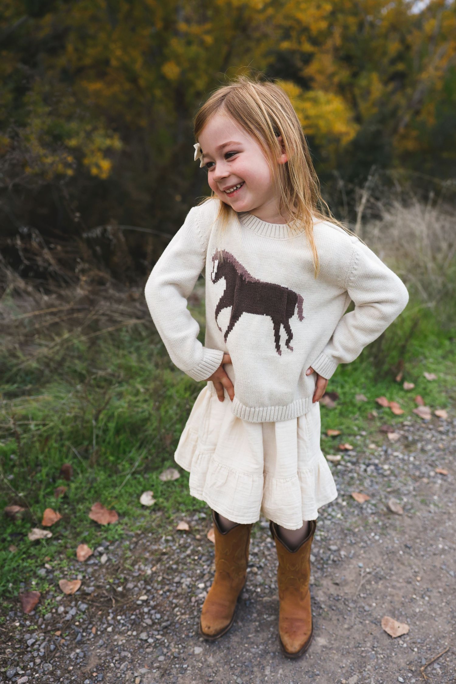 Cozy white sweater with horse design paired with brown boots on gravel path.