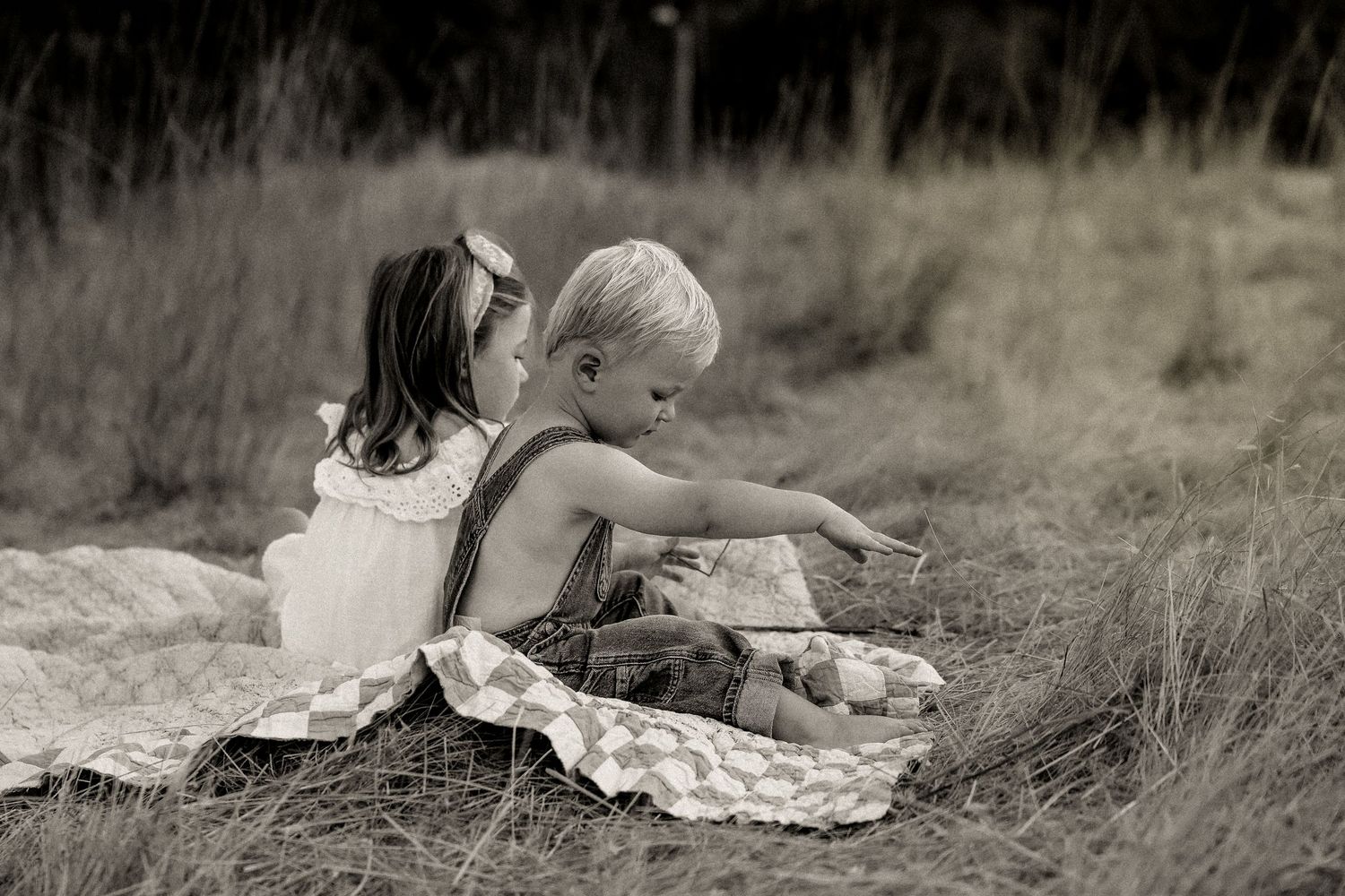 Children rest on picnic blanket in monochrome outdoor scene.