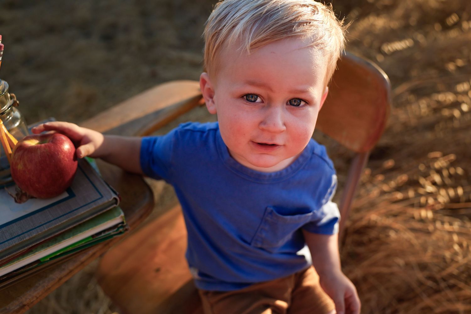 Child wearing blue shirt plays with vintage props in sun-drenched field.