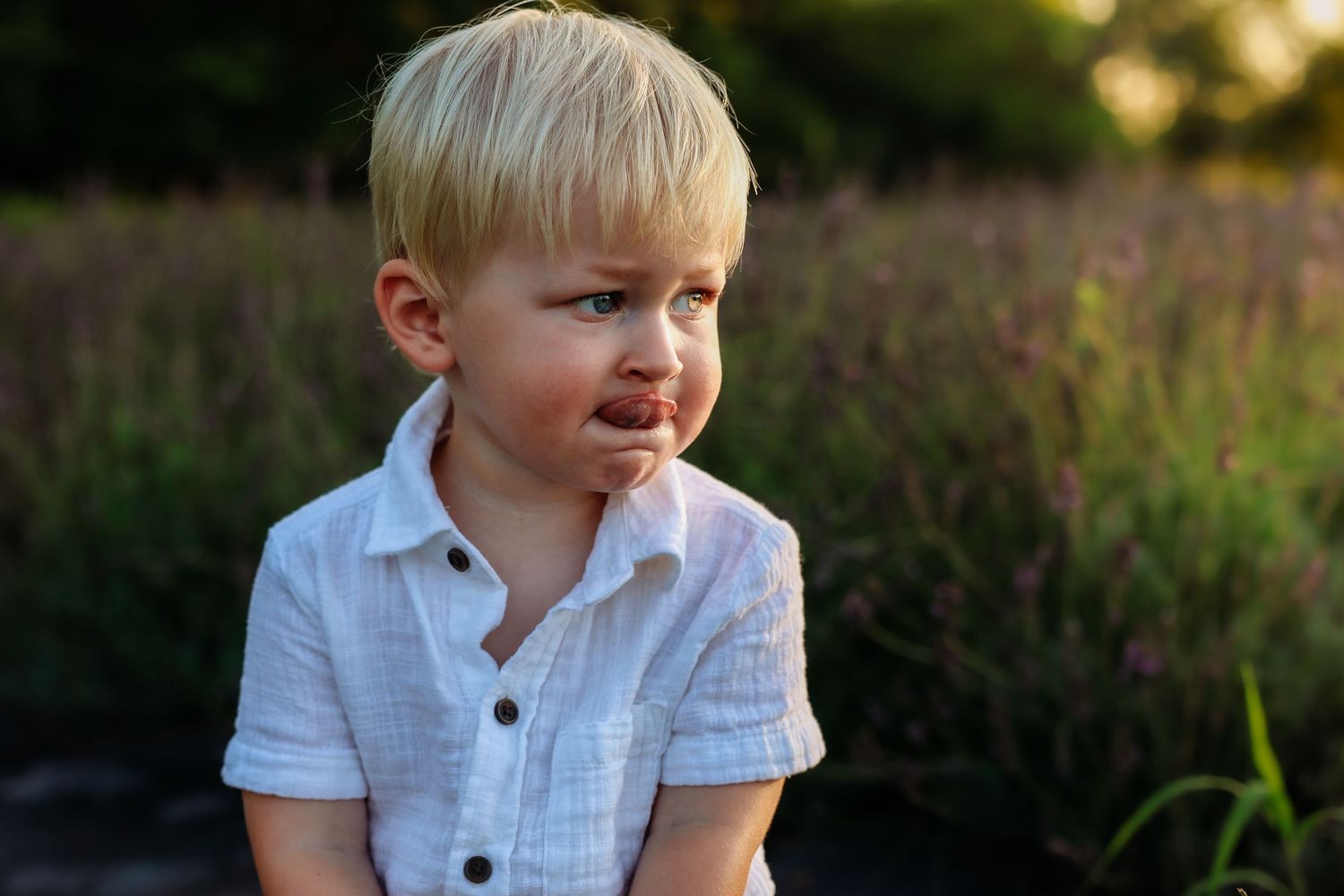 A child in a white button-down shirt sitting outdoors during golden hour.