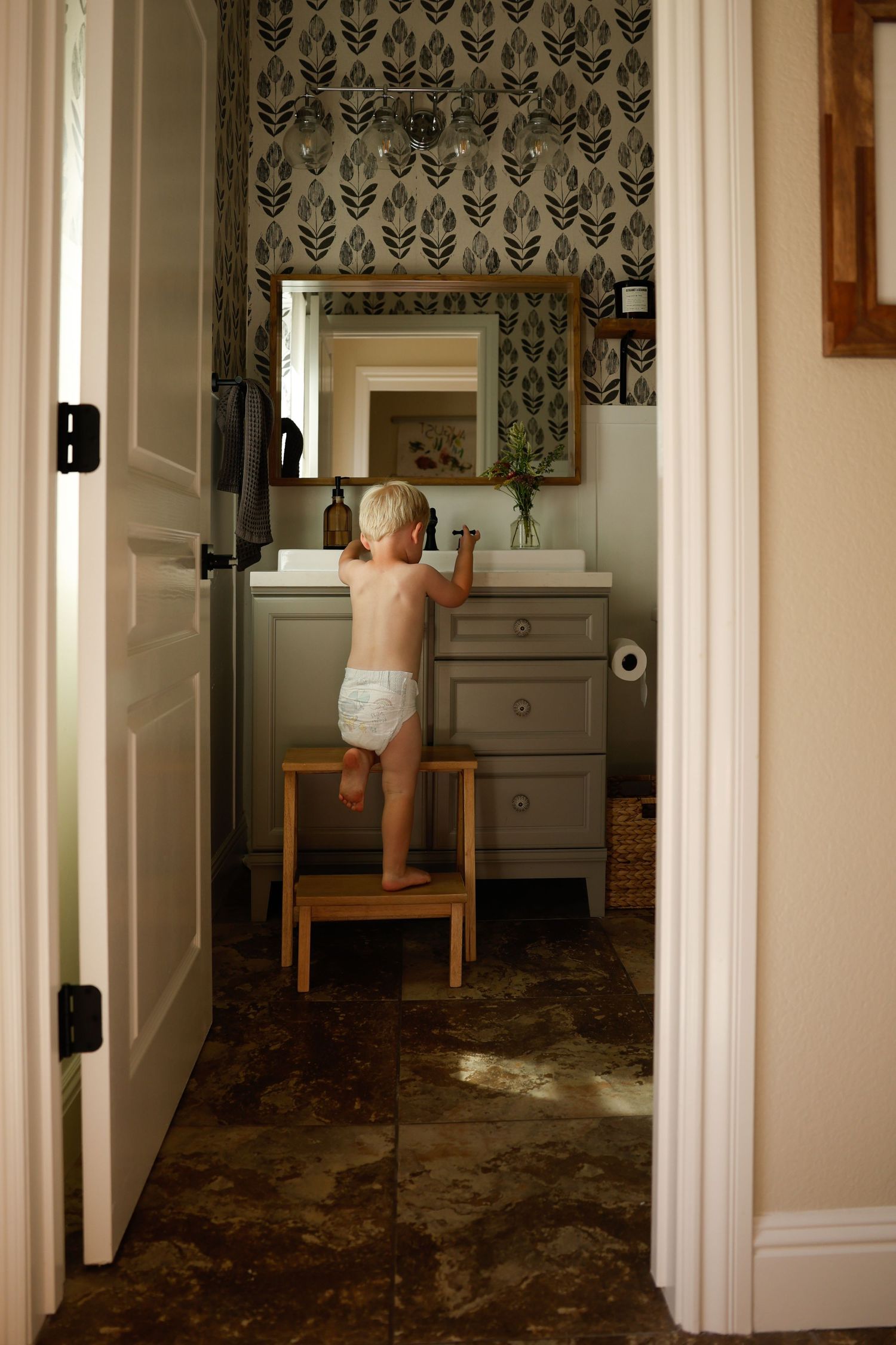 View through doorway of bathroom with feather wallpaper and gray vanity.