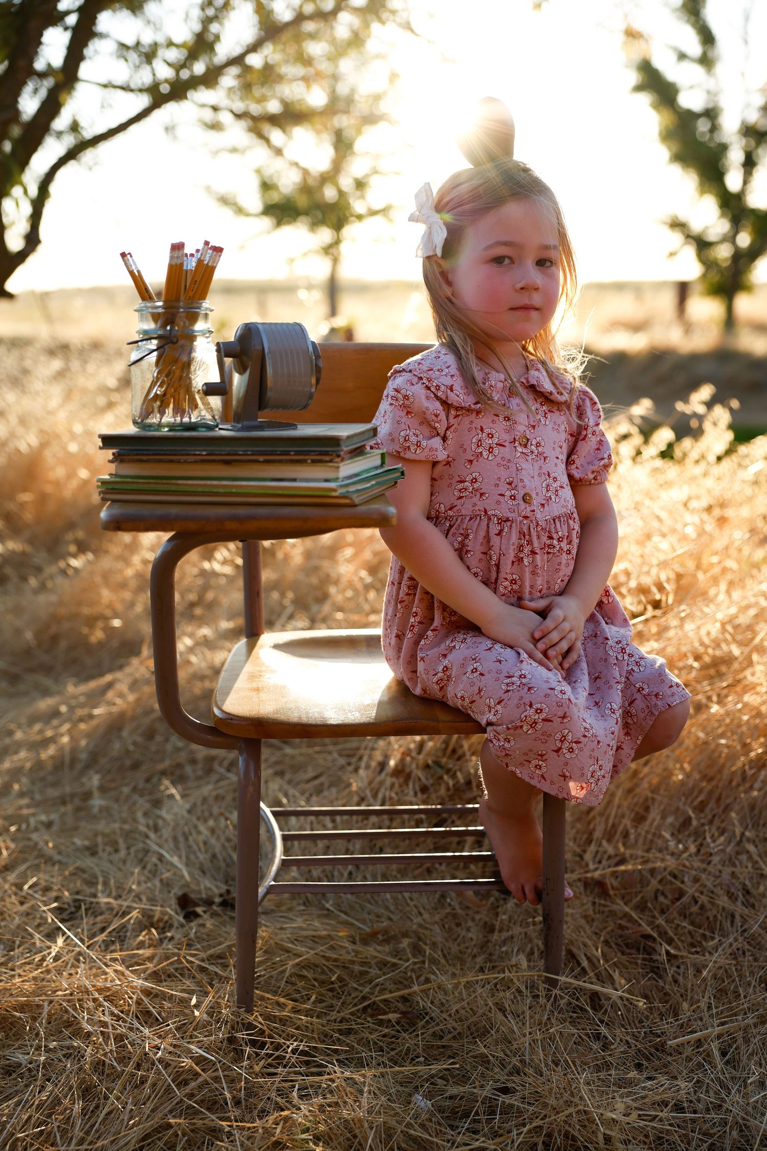 Child plays on vintage wooden desk with books and pencils in warm evening light.