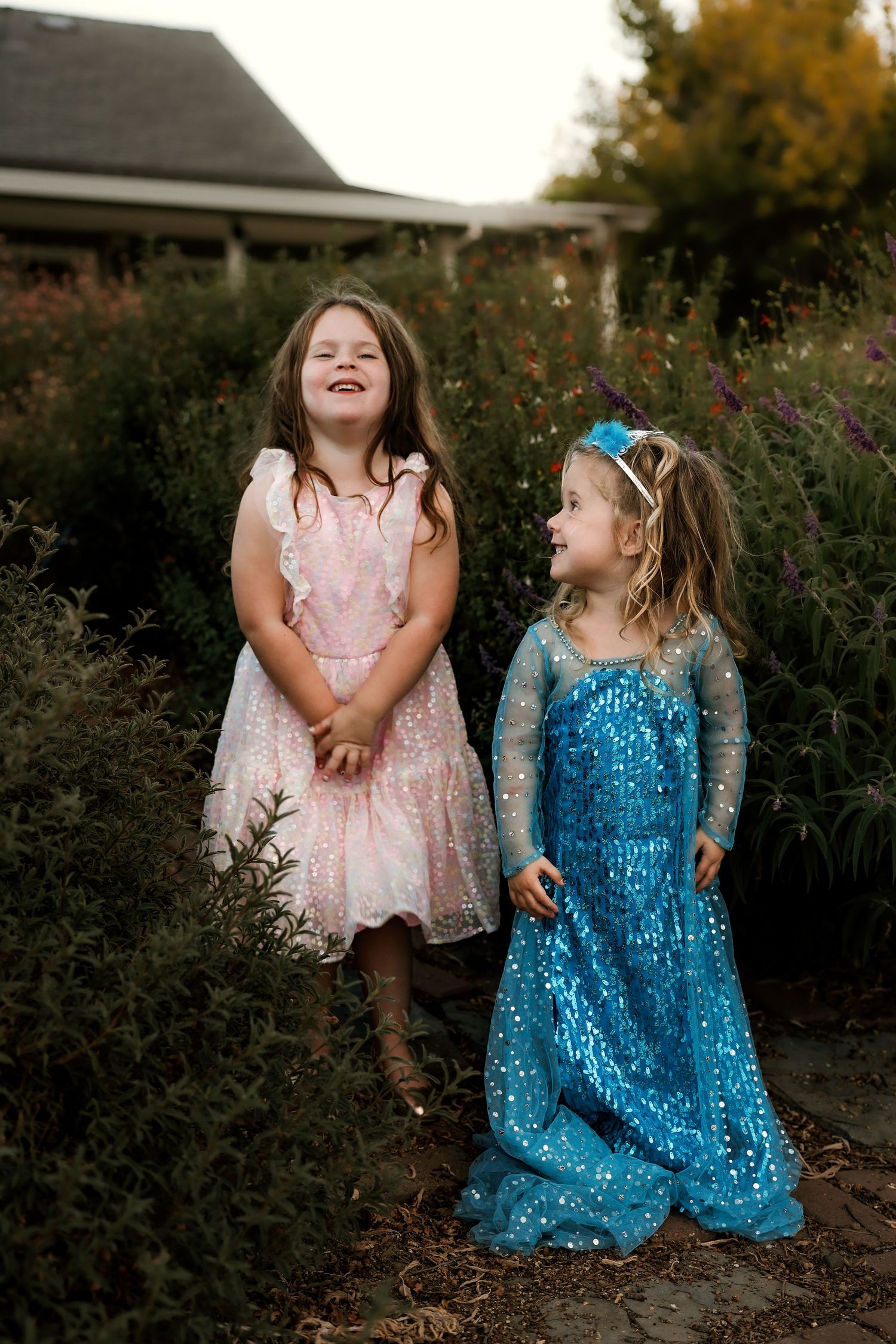 Two sparkly dresses in pink and blue shown in garden setting at dusk.