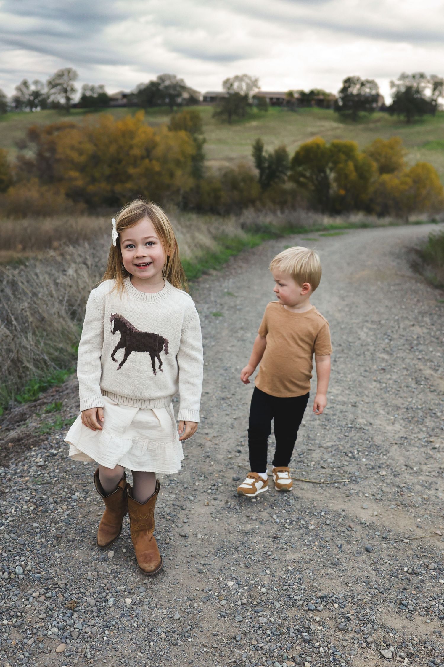 Children explore a winding gravel trail with fall colors in the background wearing matching casual outfits.
