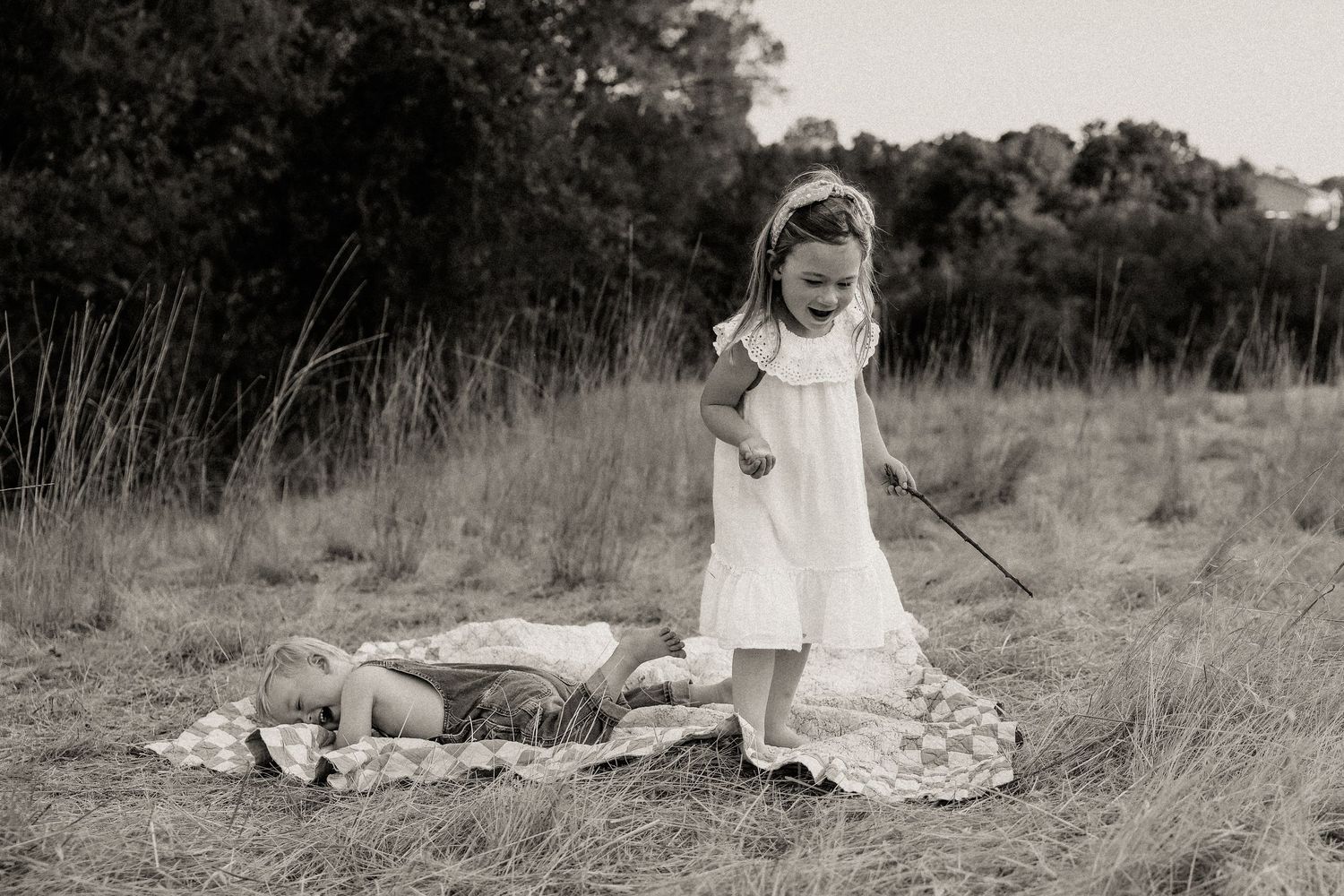 Children play together in a golden field during sunset with a blue and white checkered blanket.