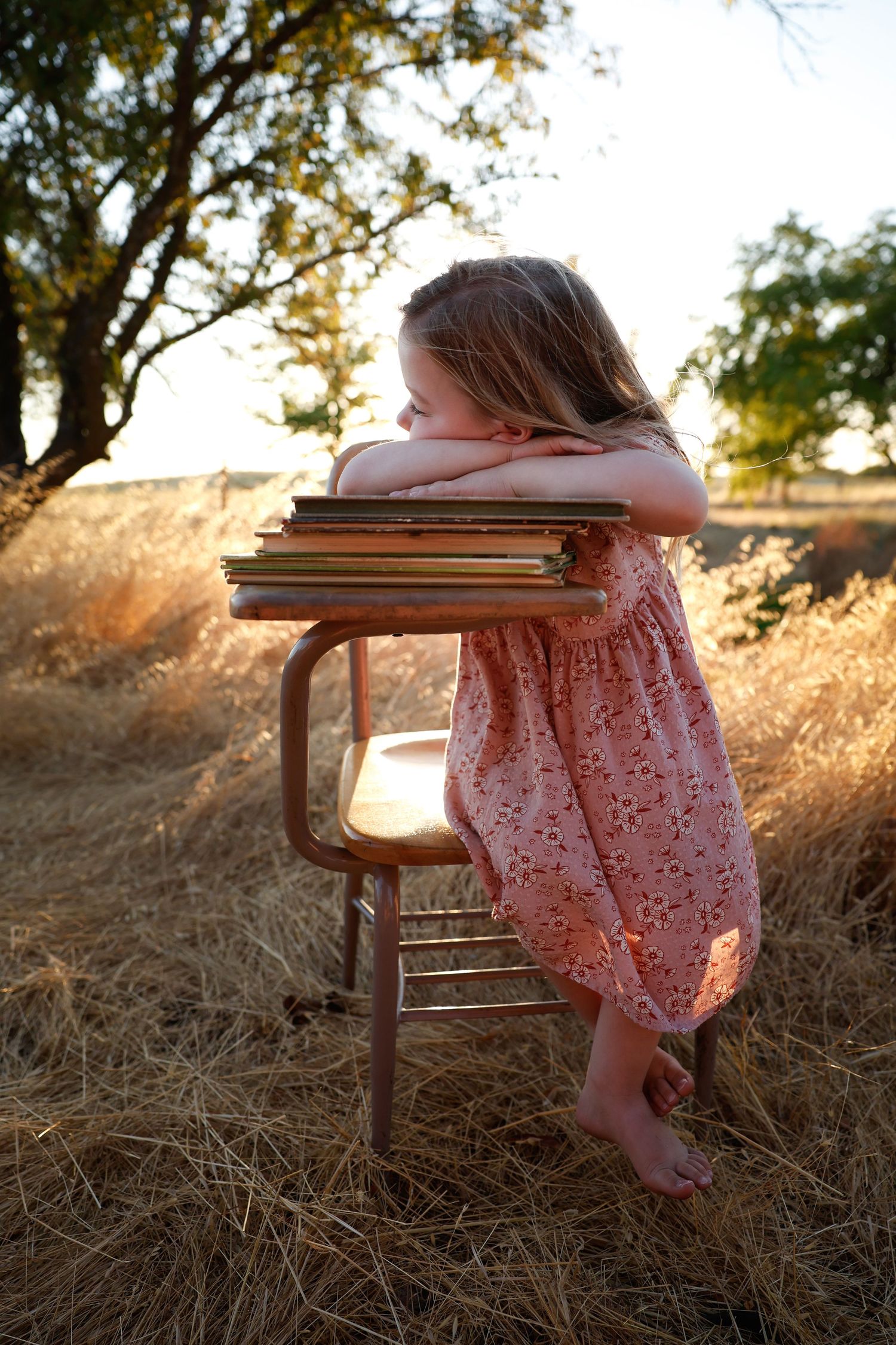 Vintage school desk scene with child in pink dress during golden hour photography.