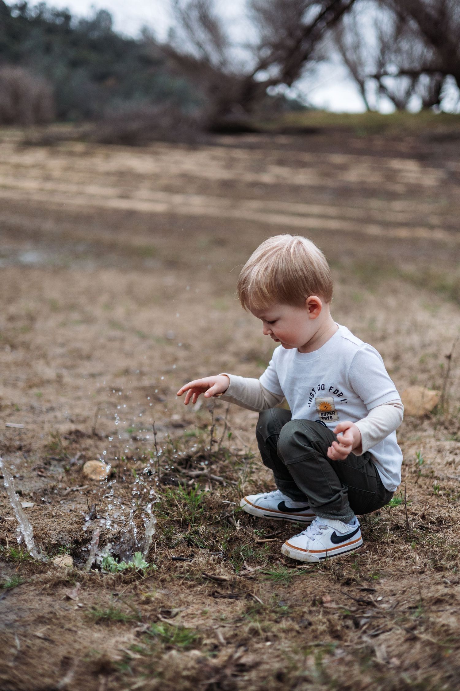 A small child explores the ground while wearing a white shirt and Nike sneakers on a dry winter landscape.