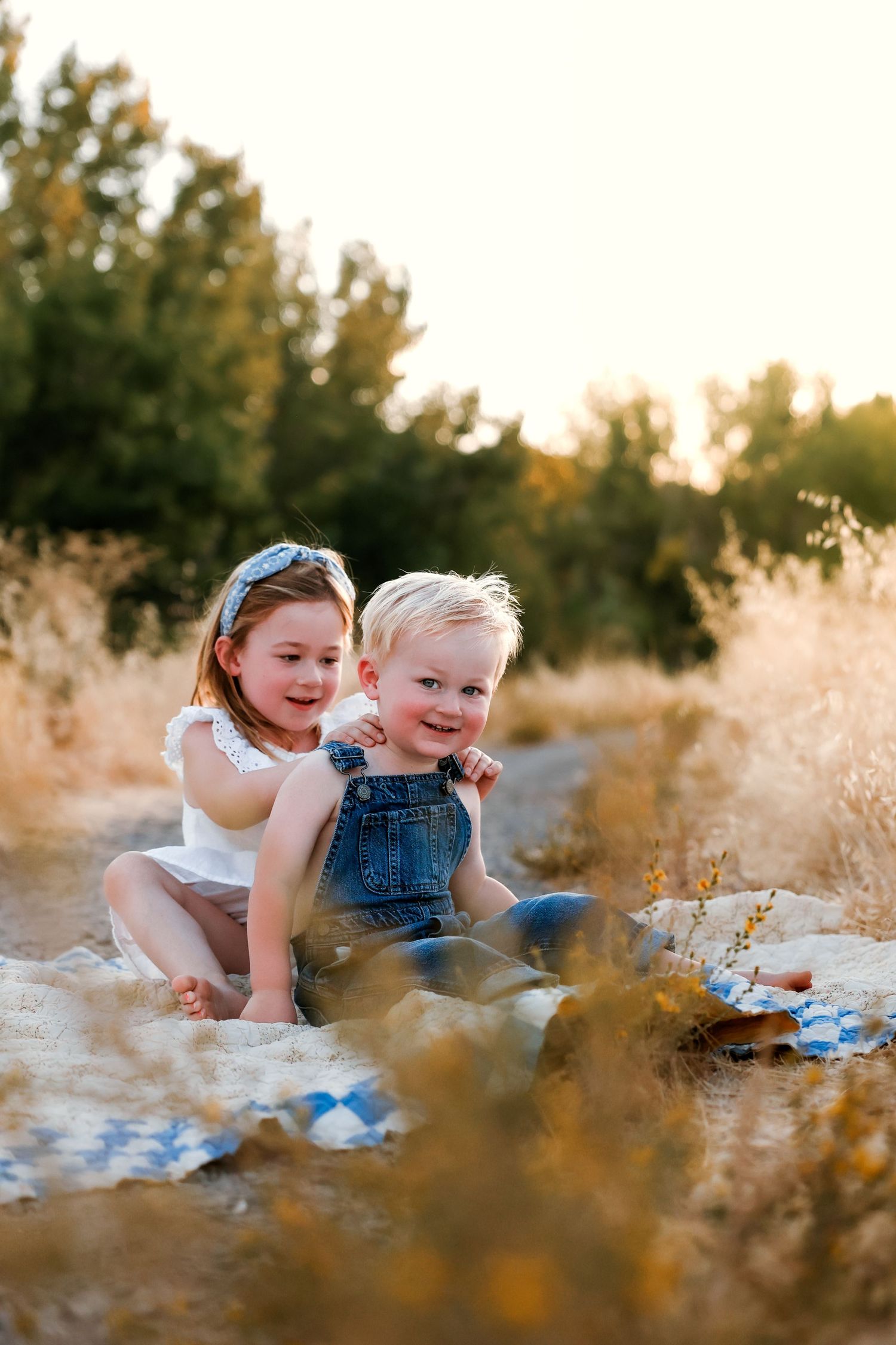 Playful interaction between children amid tall grass during golden hour photography session.