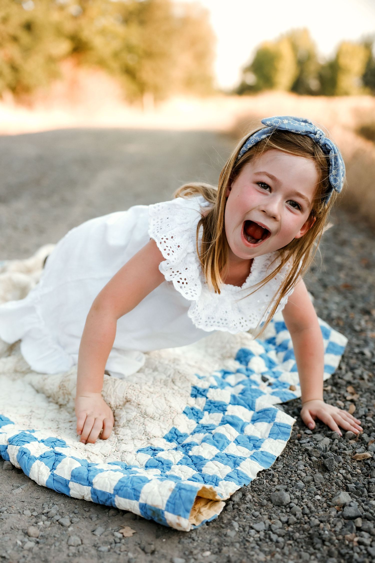 White eyelet dress spreads over blue checkered blanket on rocky ground.