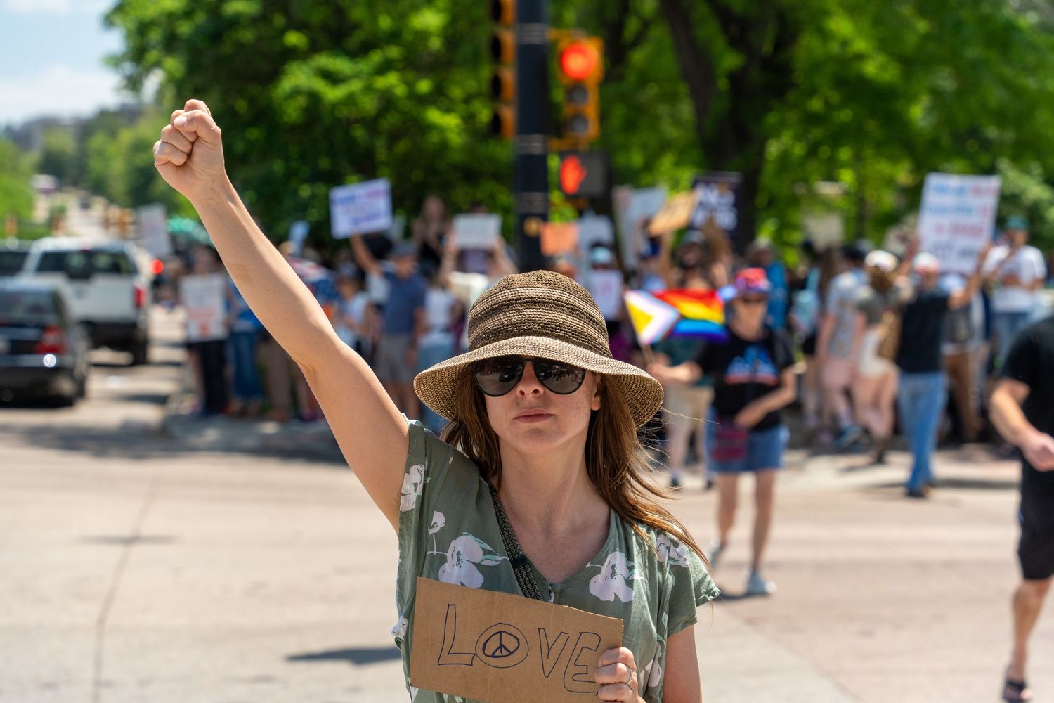 Protester raises fist while wearing sun hat at outdoor demonstration.