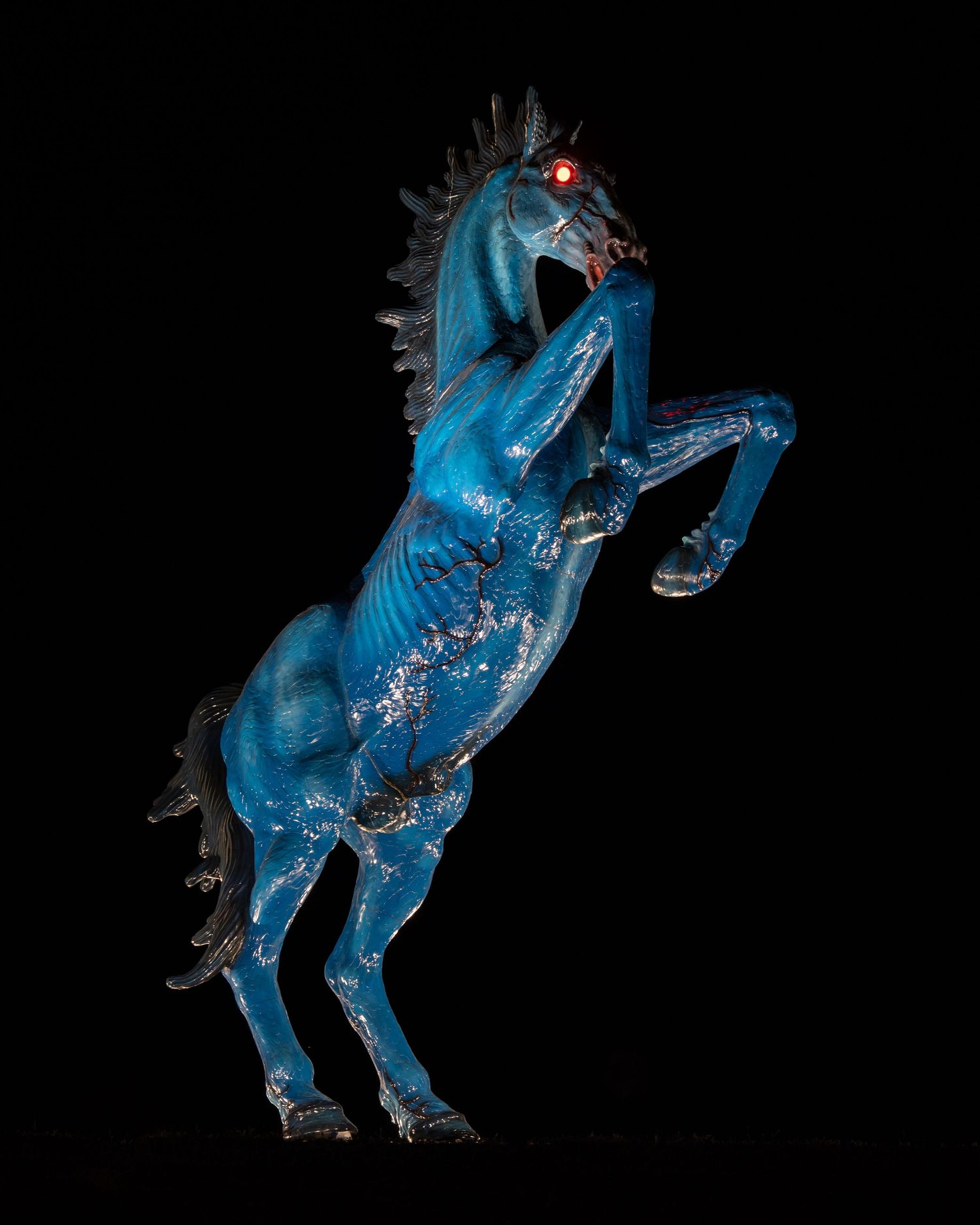 Bright blue horse statue rearing up against black background.