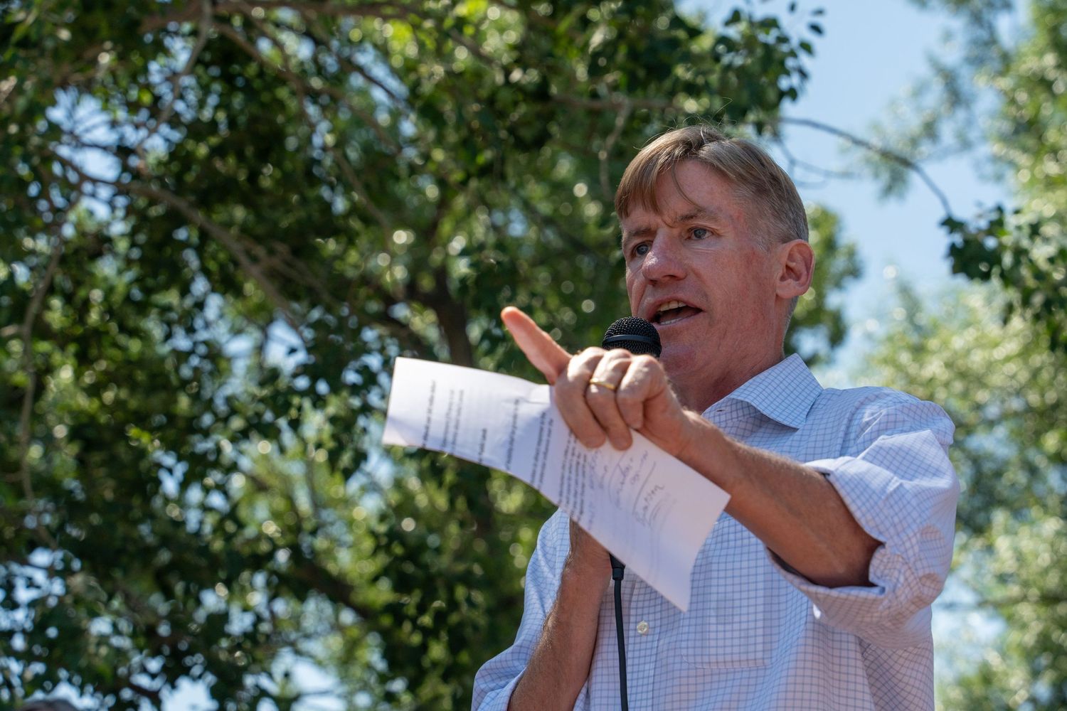 Person in white shirt pointing while speaking at a protest.