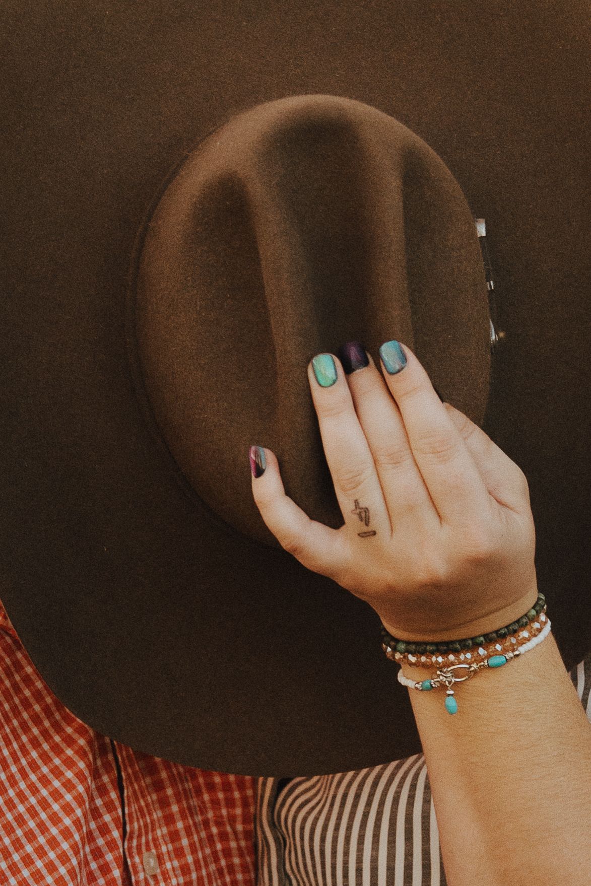 A brown felt cowboy hat is held by hands wearing turquoise jewelry against a rustic background.