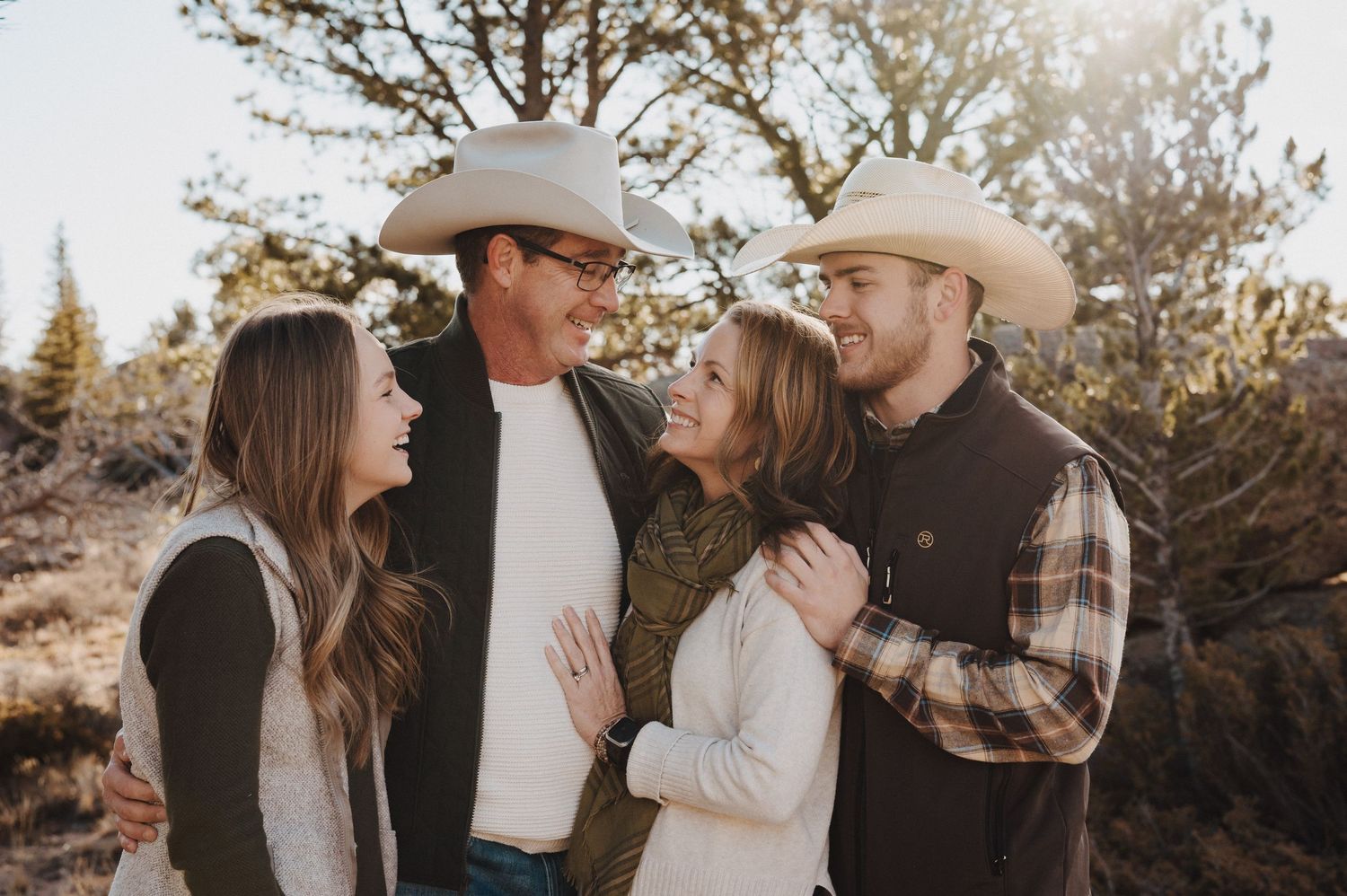 A family embraces during a golden hour photo session in a natural outdoor setting with trees in the background.