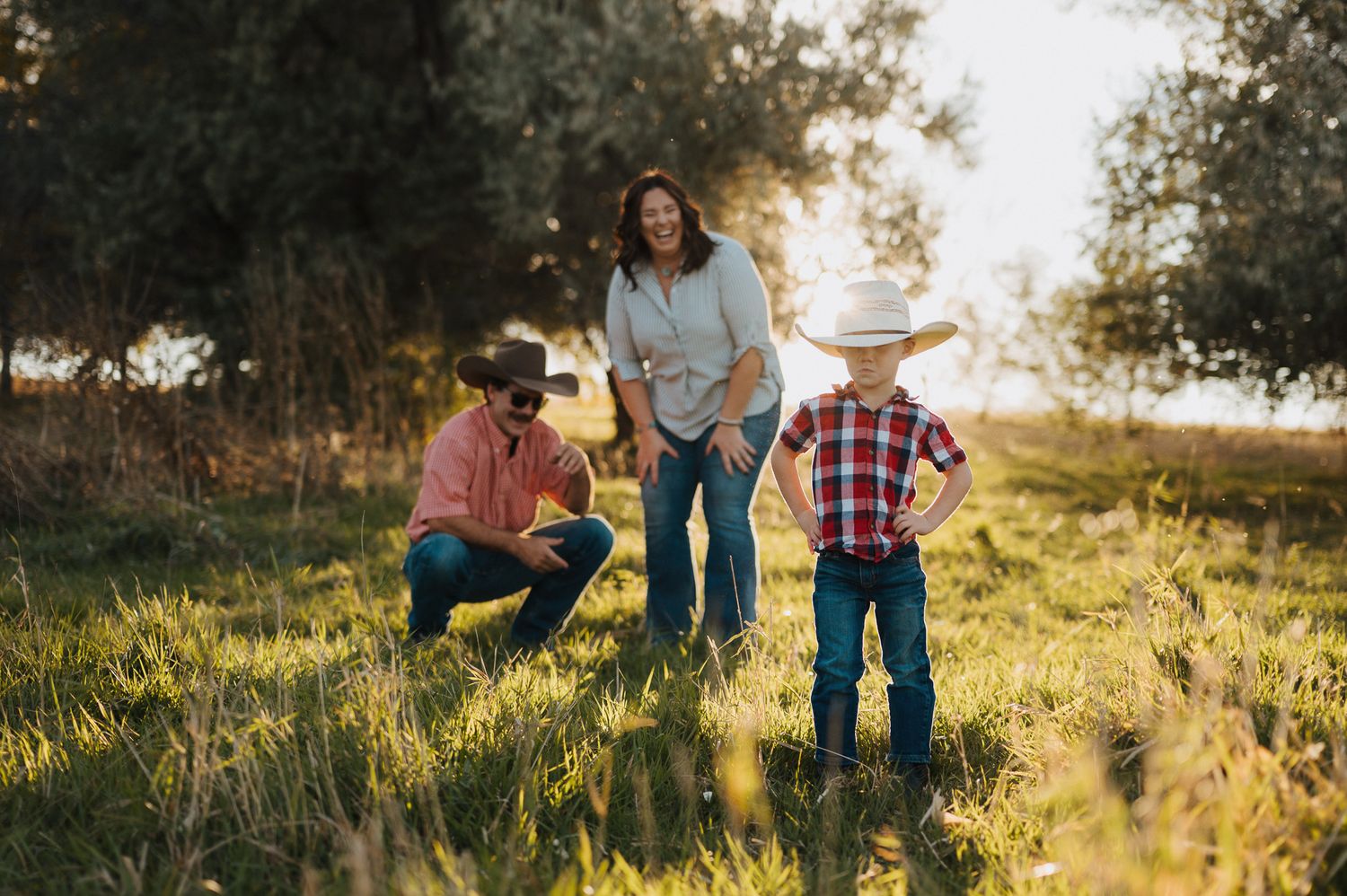 Family enjoying golden hour in a grassy meadow during sunset, silhouetted against warm evening light.