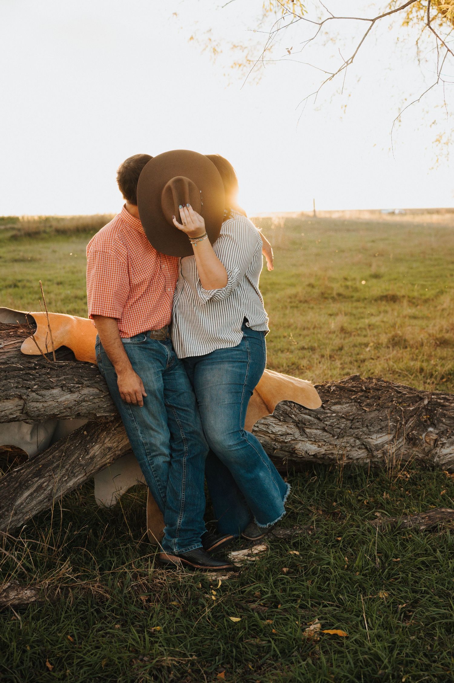A wife holds a cowboy hat over her and her husband's face as they kiss in front of a tree in a field in Lyman, Nebraska.