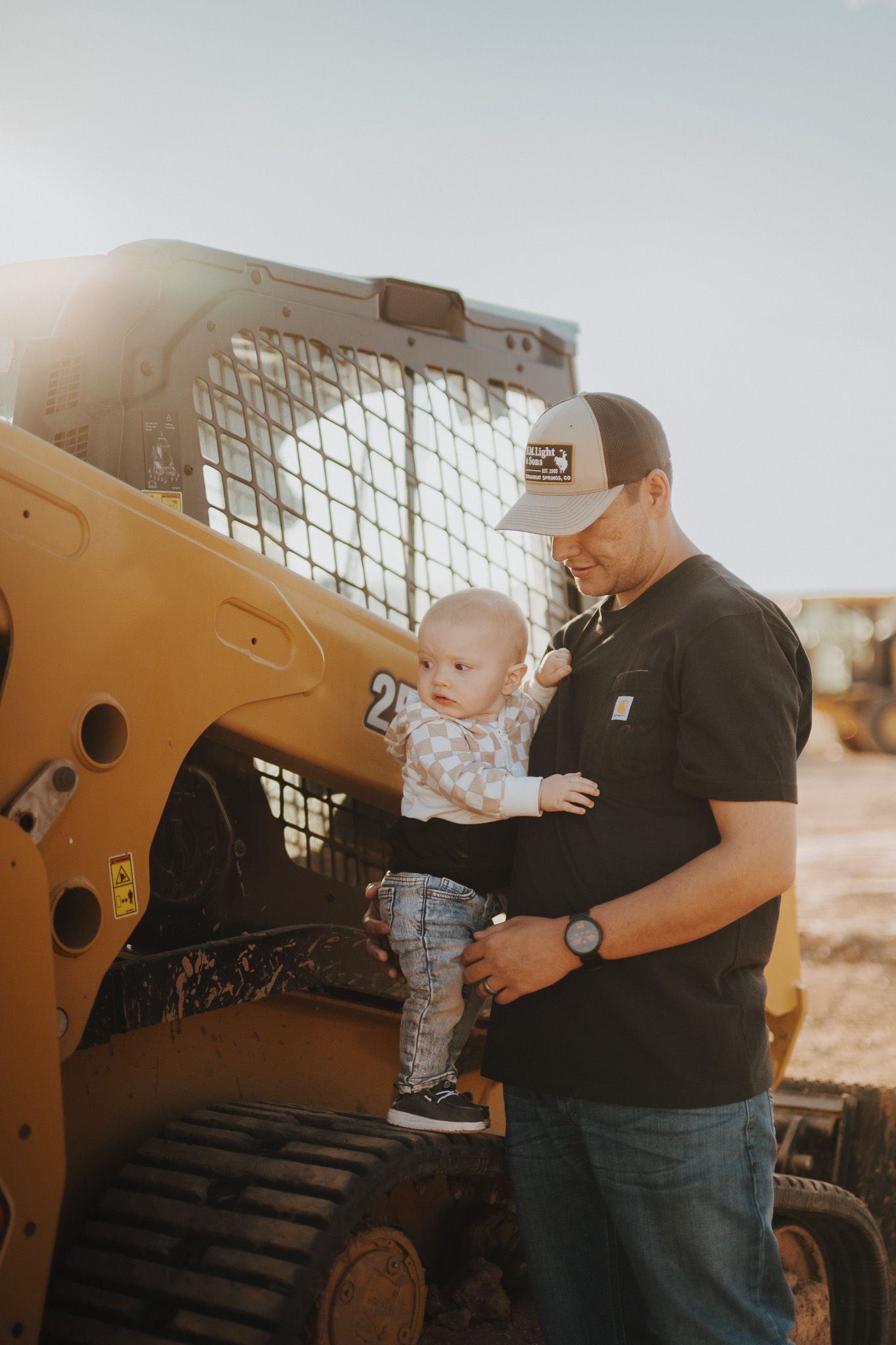 A child explores a yellow construction equipment vehicle while an adult supervises outdoors.