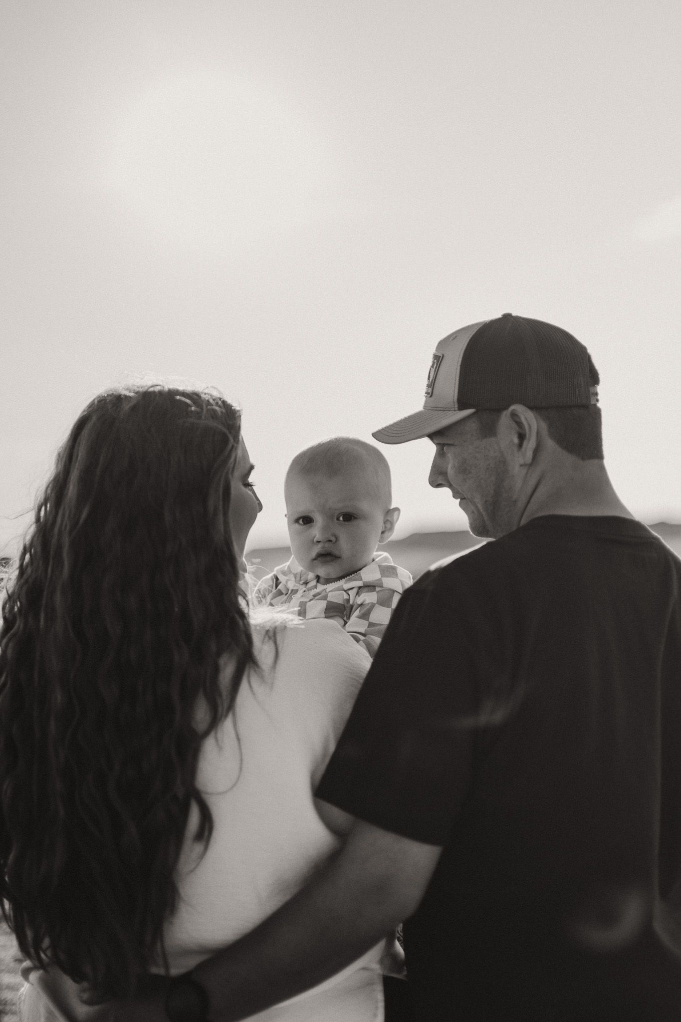 A black and white photo showing a couple embracing and admiring their toddler son.