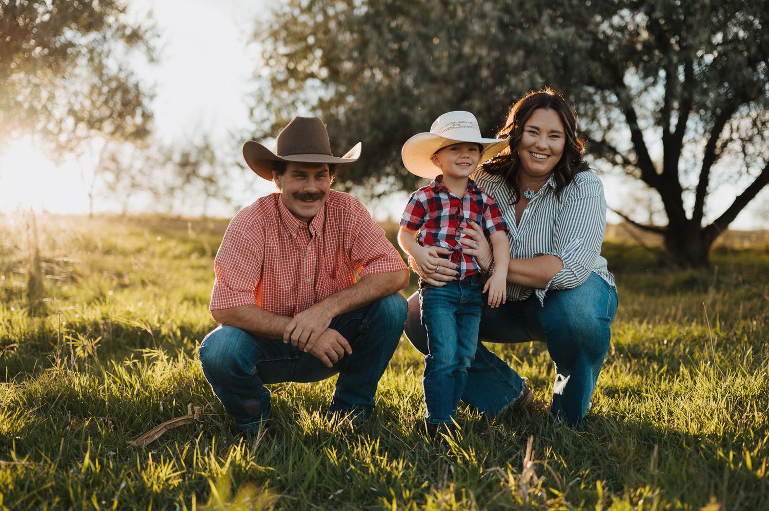 A family in western attire poses together on a grassy hill during golden hour sunset.