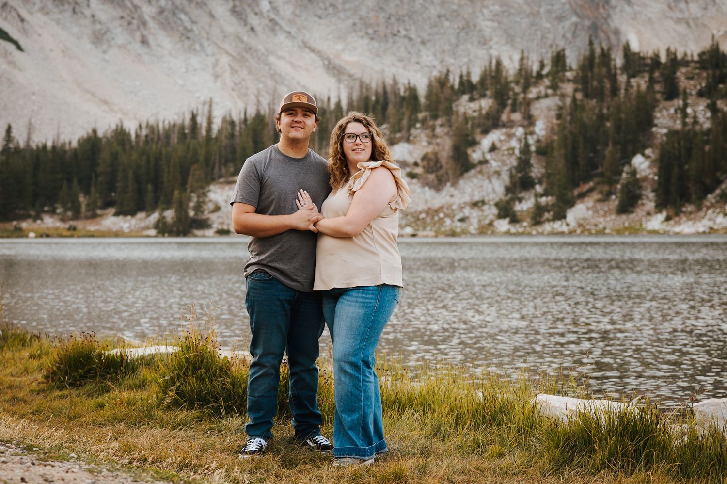 A man and a woman standing next to each other and posing in front of Mirror Lake in Wyoming.