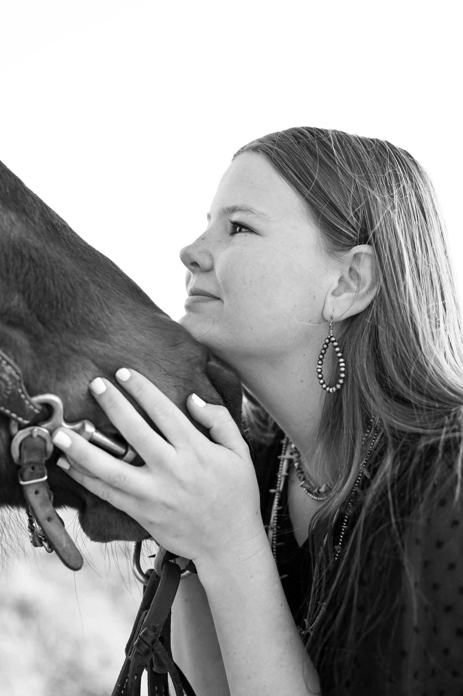 A black and white photo showing a tender moment between a girl and a horse in profile view.