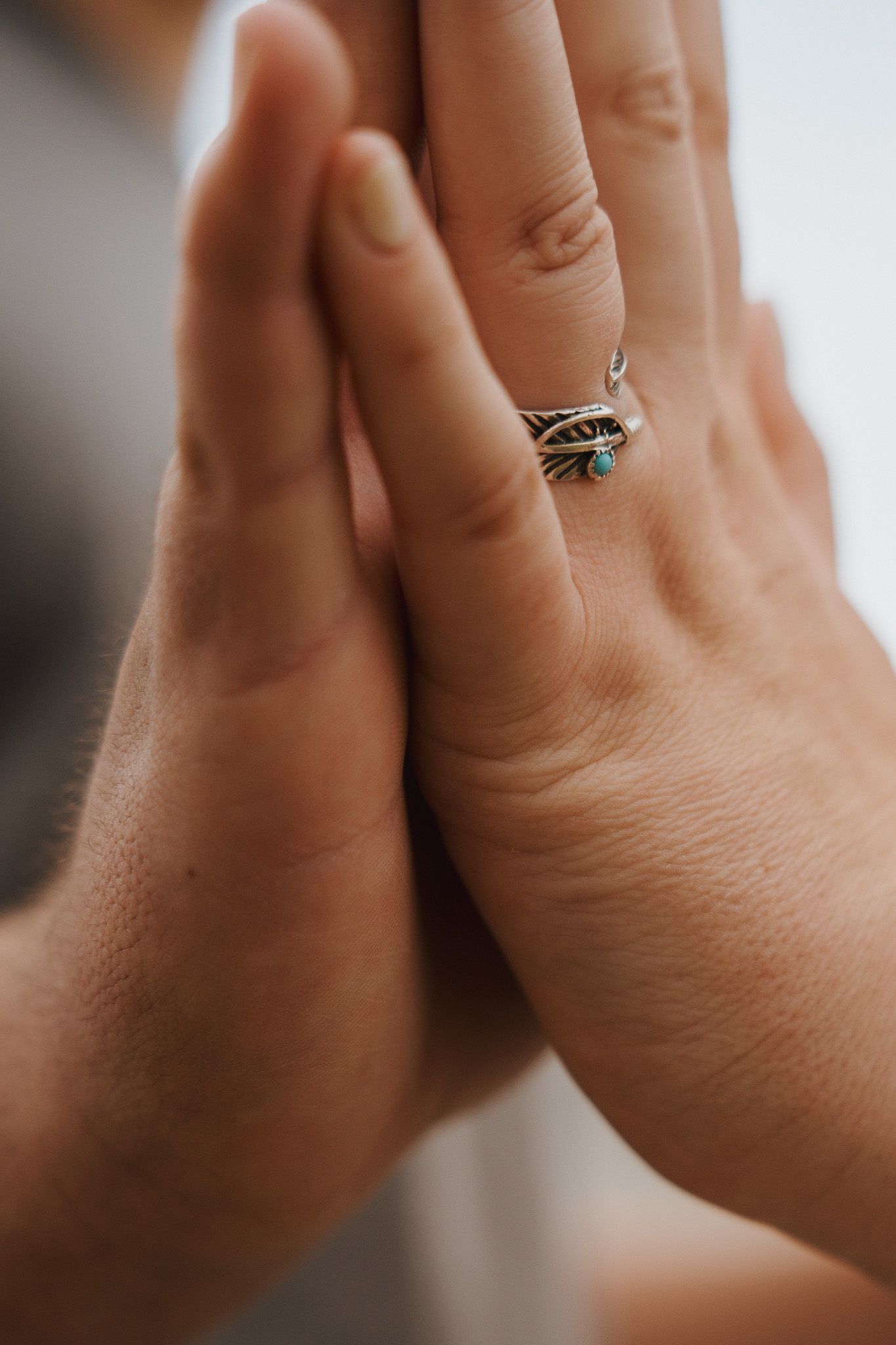 Two hands pressed together, with a silver ring on one of the fingers.