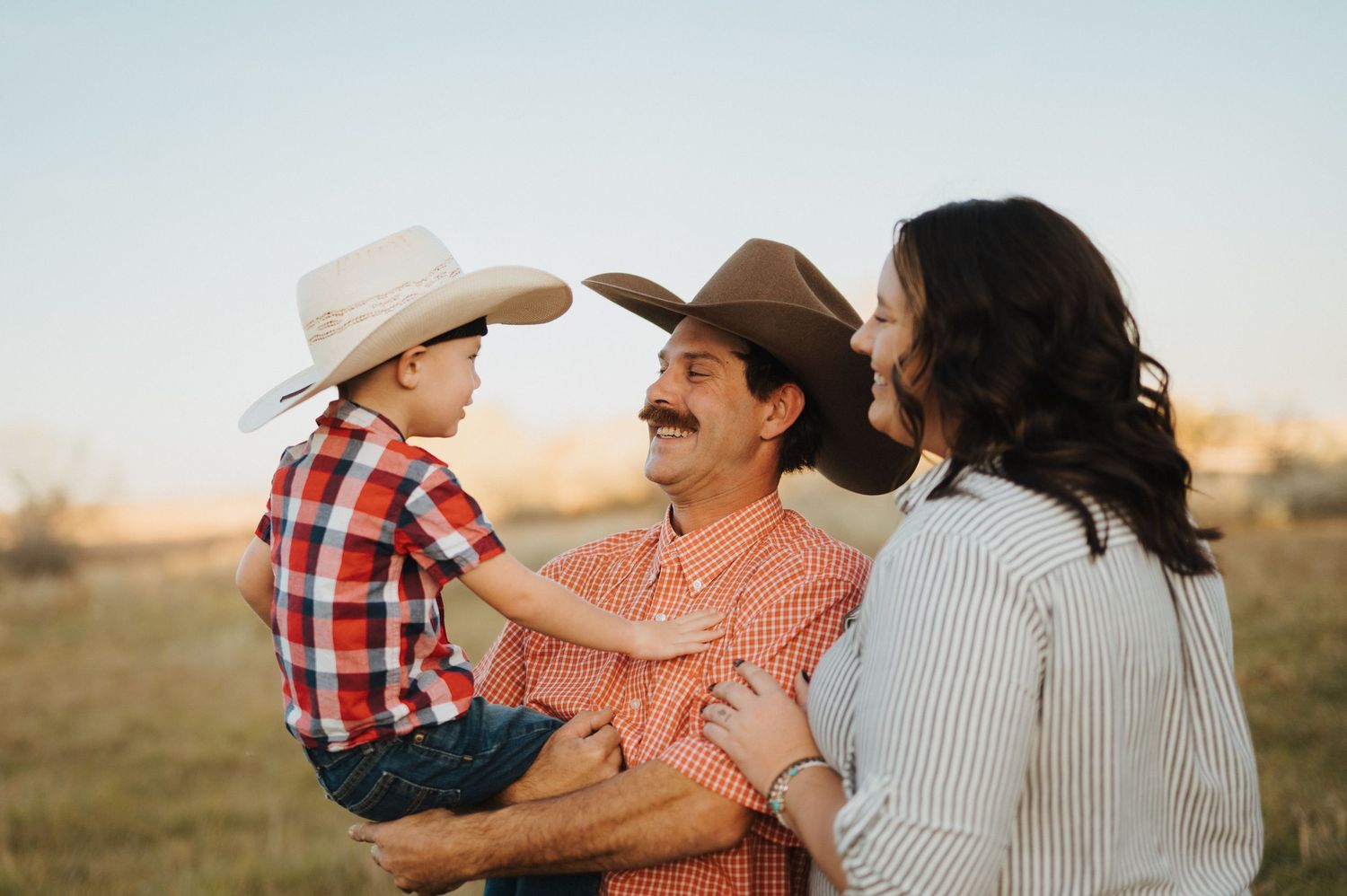 A family shares a joyful moment together in a field during golden hour wearing western style clothing.
