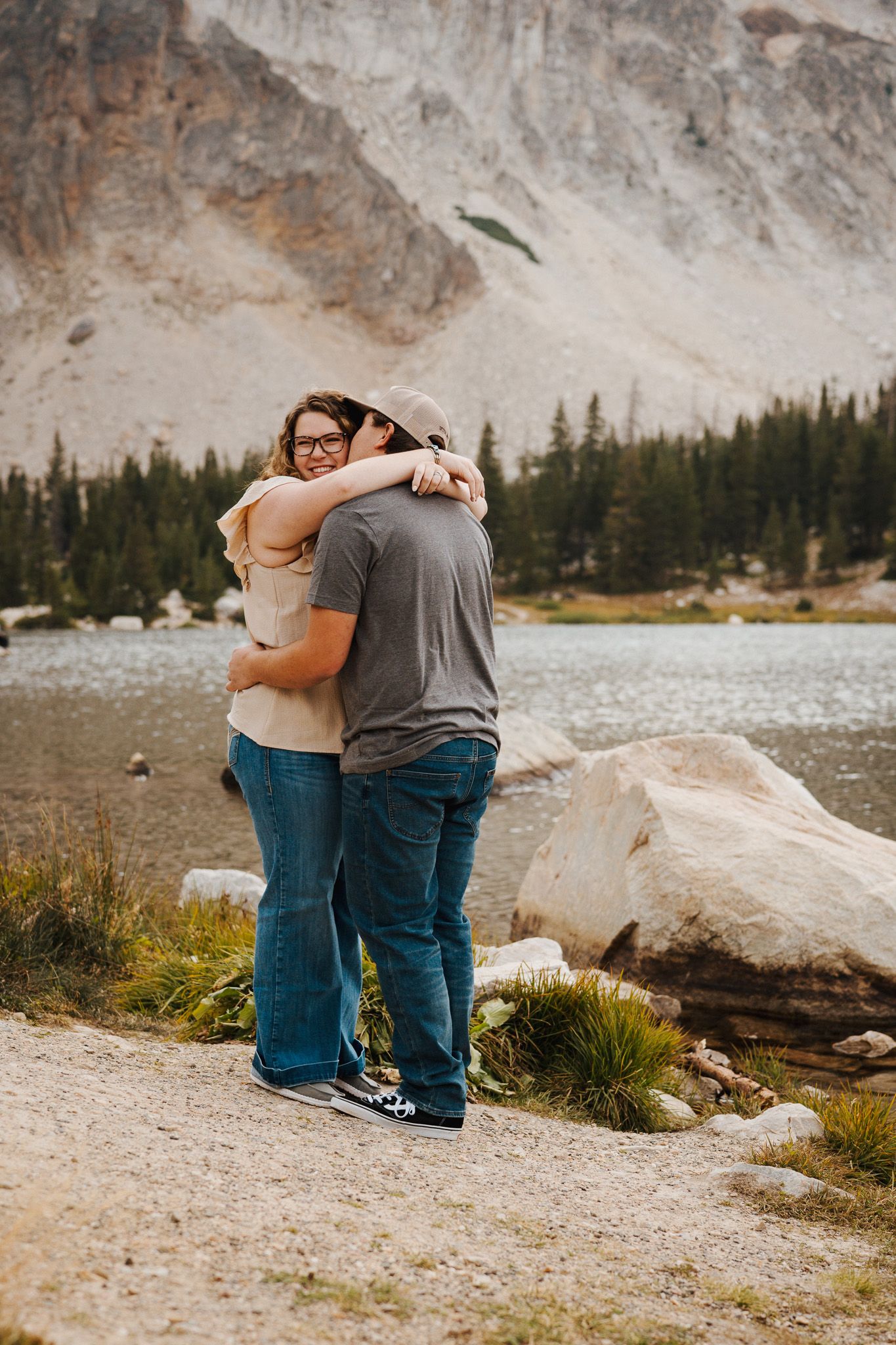 A man and a woman hug in front of Mirror Lake, with Medicine Bow Peak in the background.