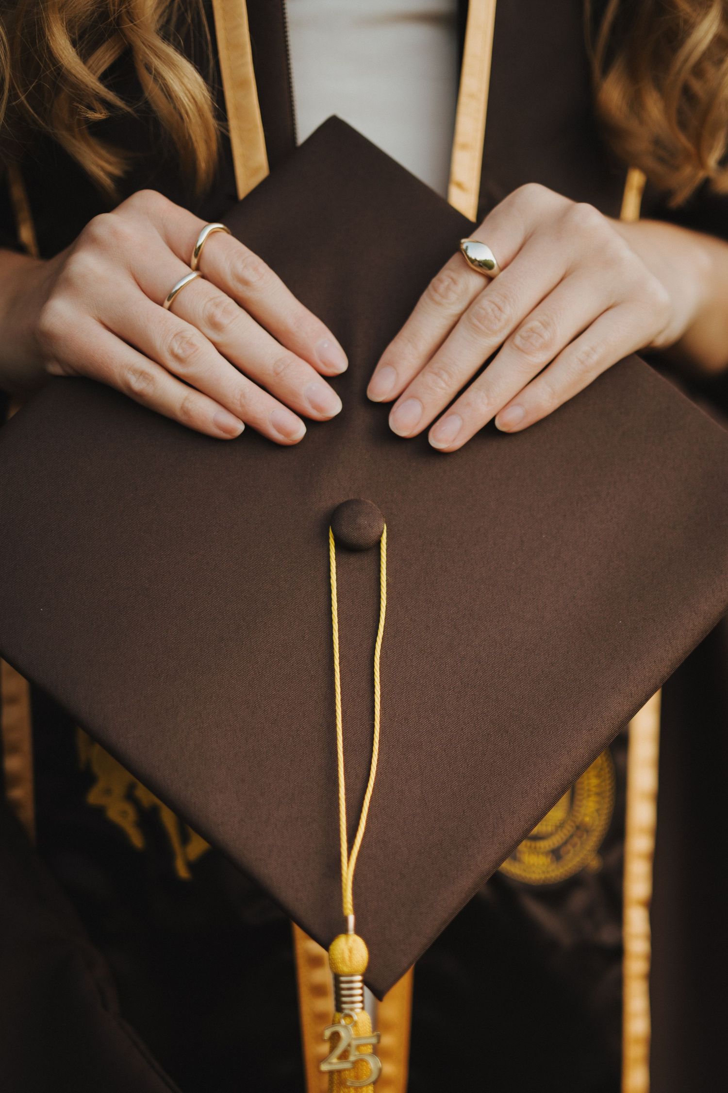 Close-up sequence showing hands adjusting a brown graduation cap with gold tassel.