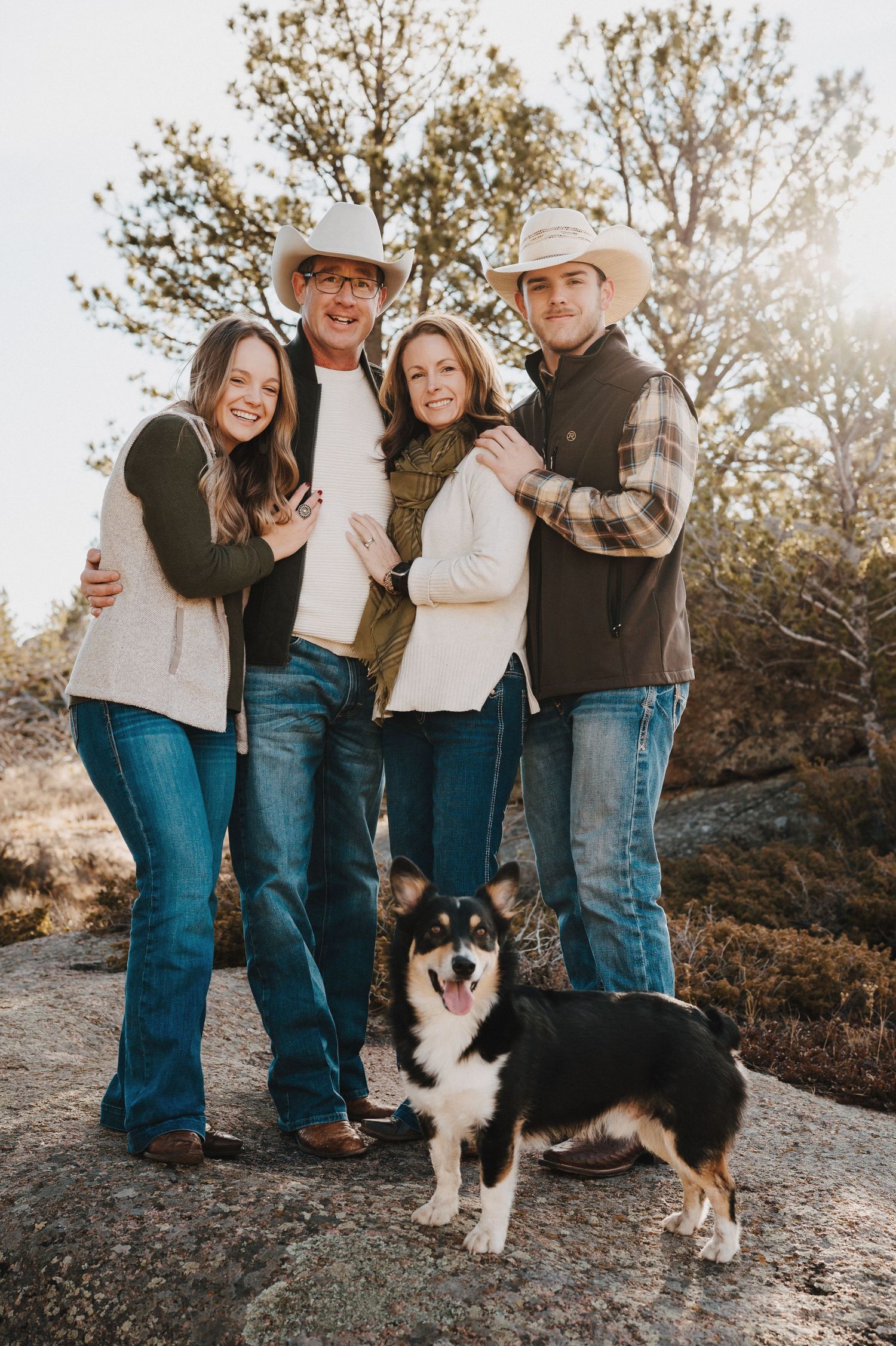 Family poses outdoors in casual western attire with their dog on a sunny afternoon.