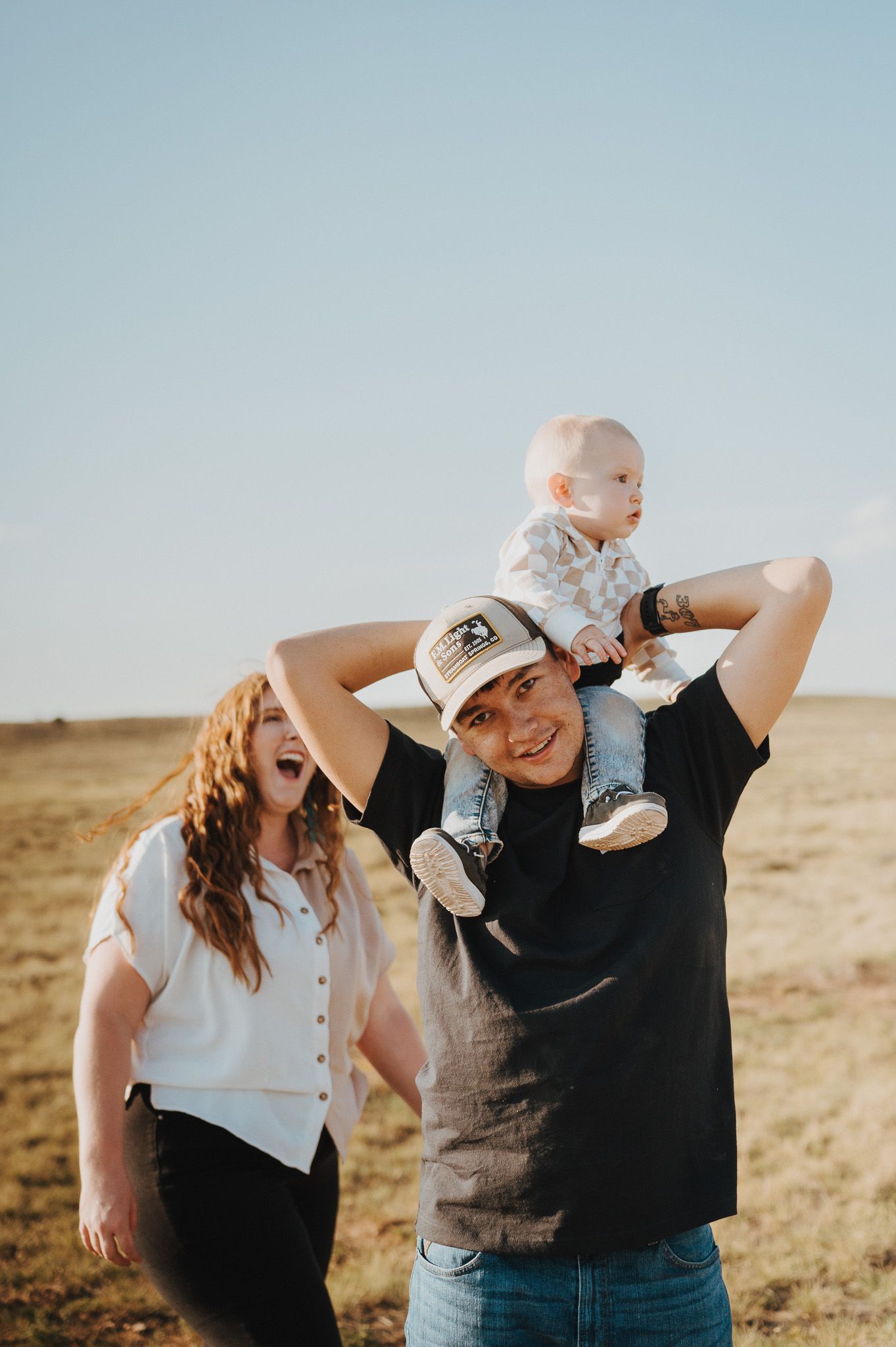 A couple laughs and poses playfully together in a series of candid shots taken in an open field at sunset.