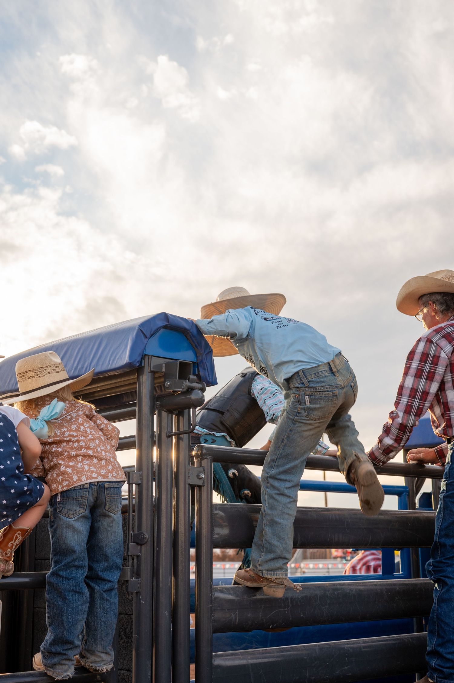 A young boy wearing a cowboy hat climbs over the top of a bucking chute at a rodeo in Laramie, Wyoming.