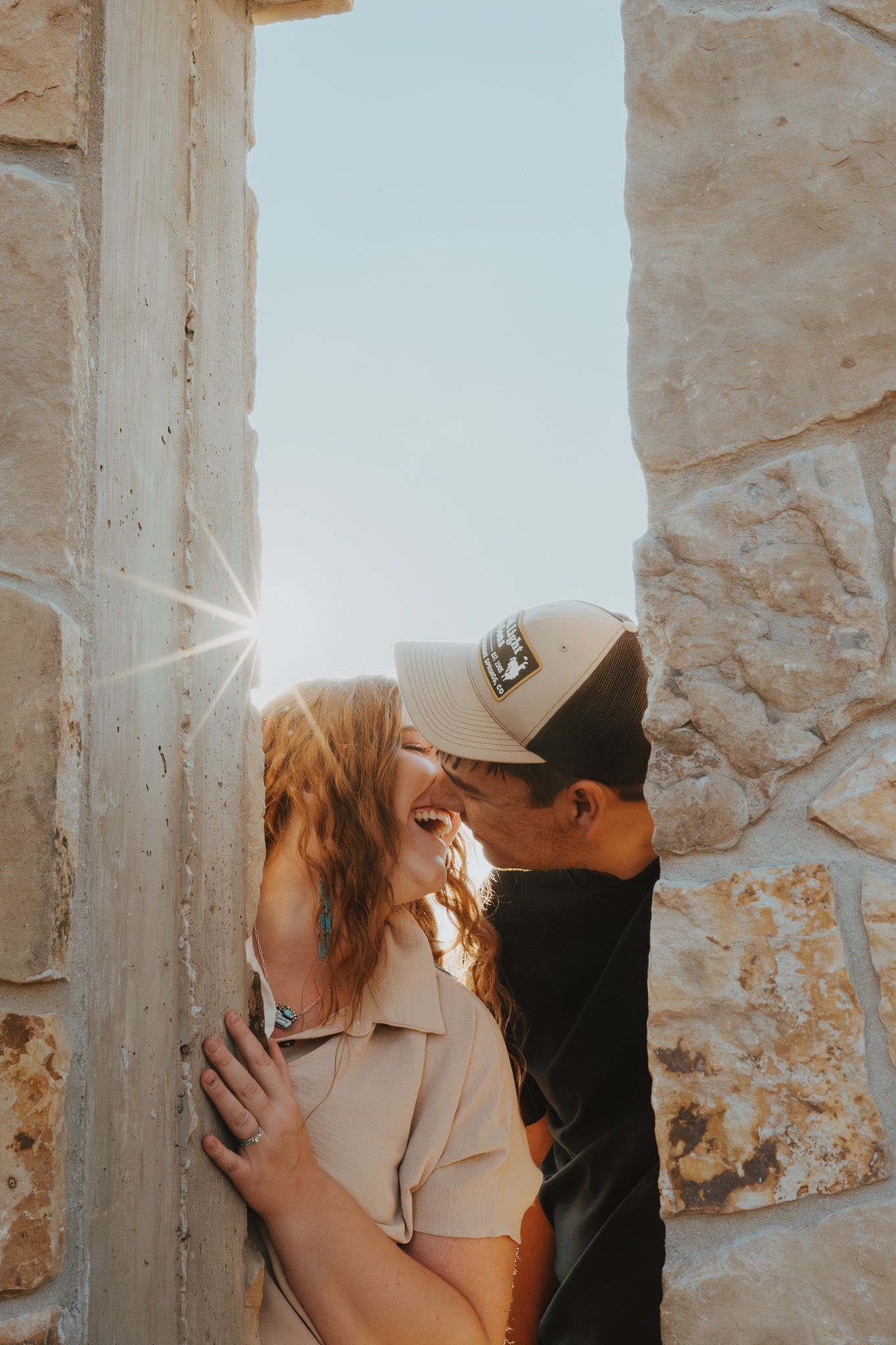 A husband and wife smiling with their faces close together, framed by a stone window.