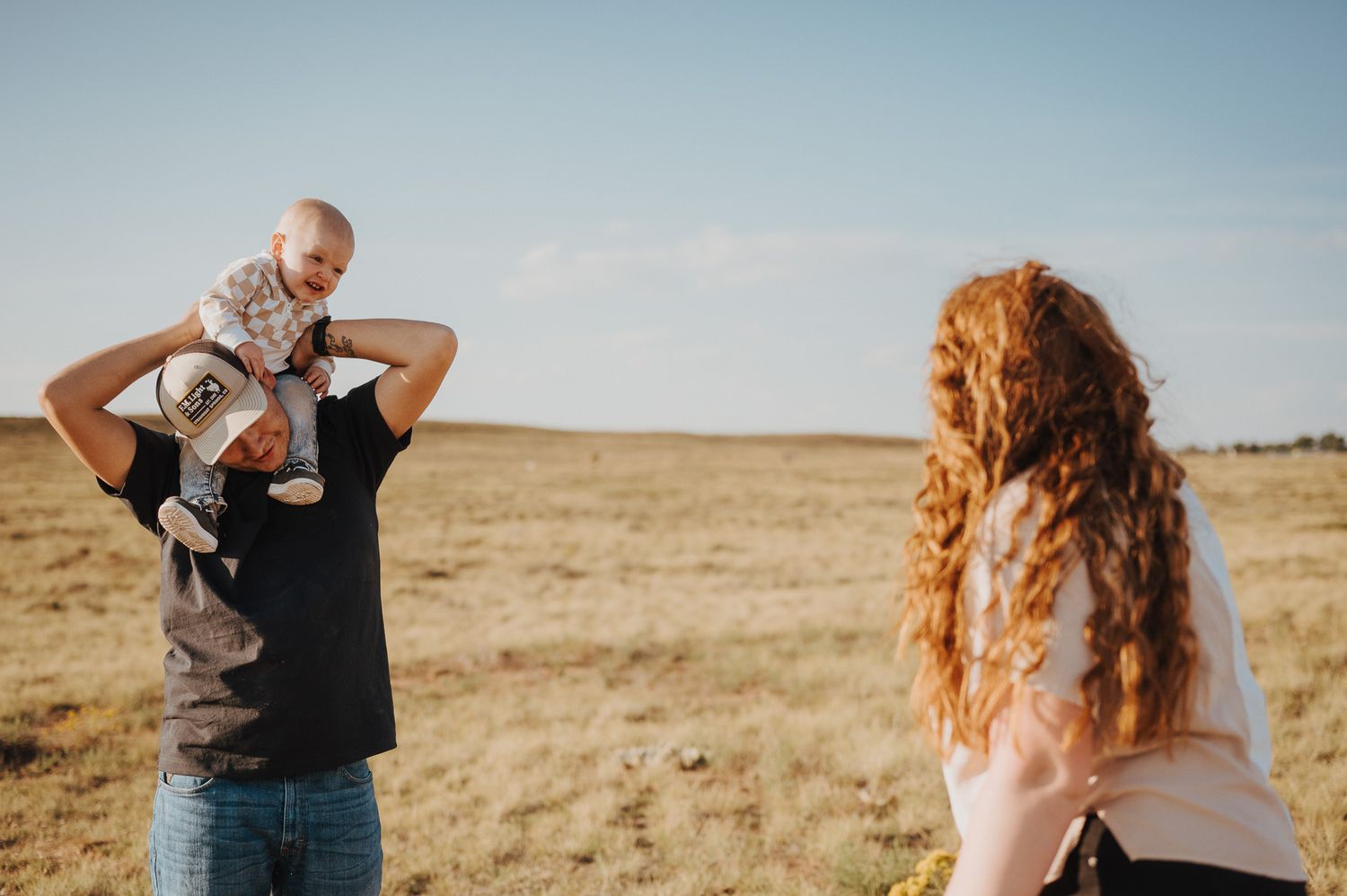 A couple playfully interacting with their toddler son in a grassy field in Laramie, Wyoming.