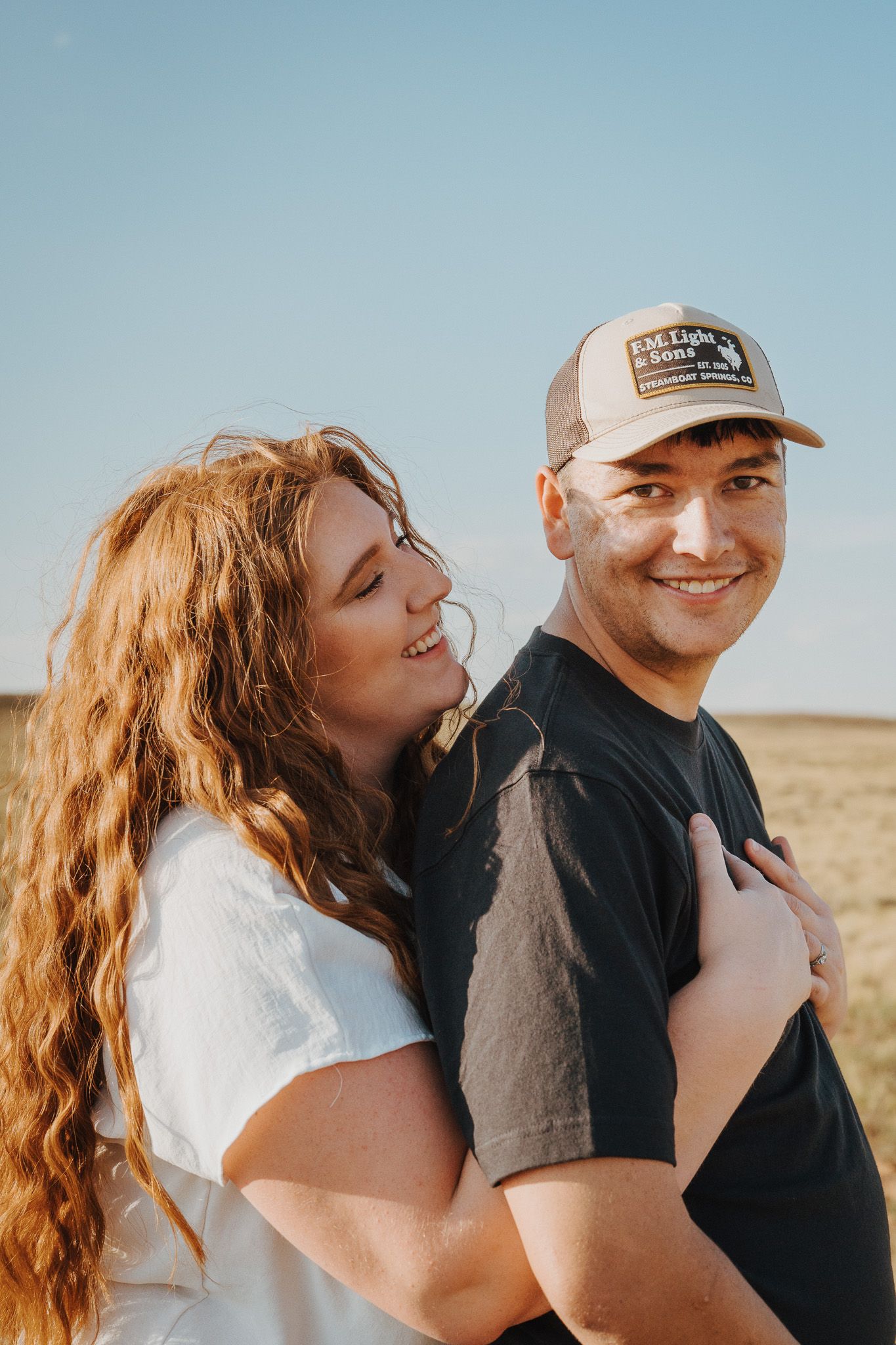A wife embracing her husband from behind as her husband smiles.