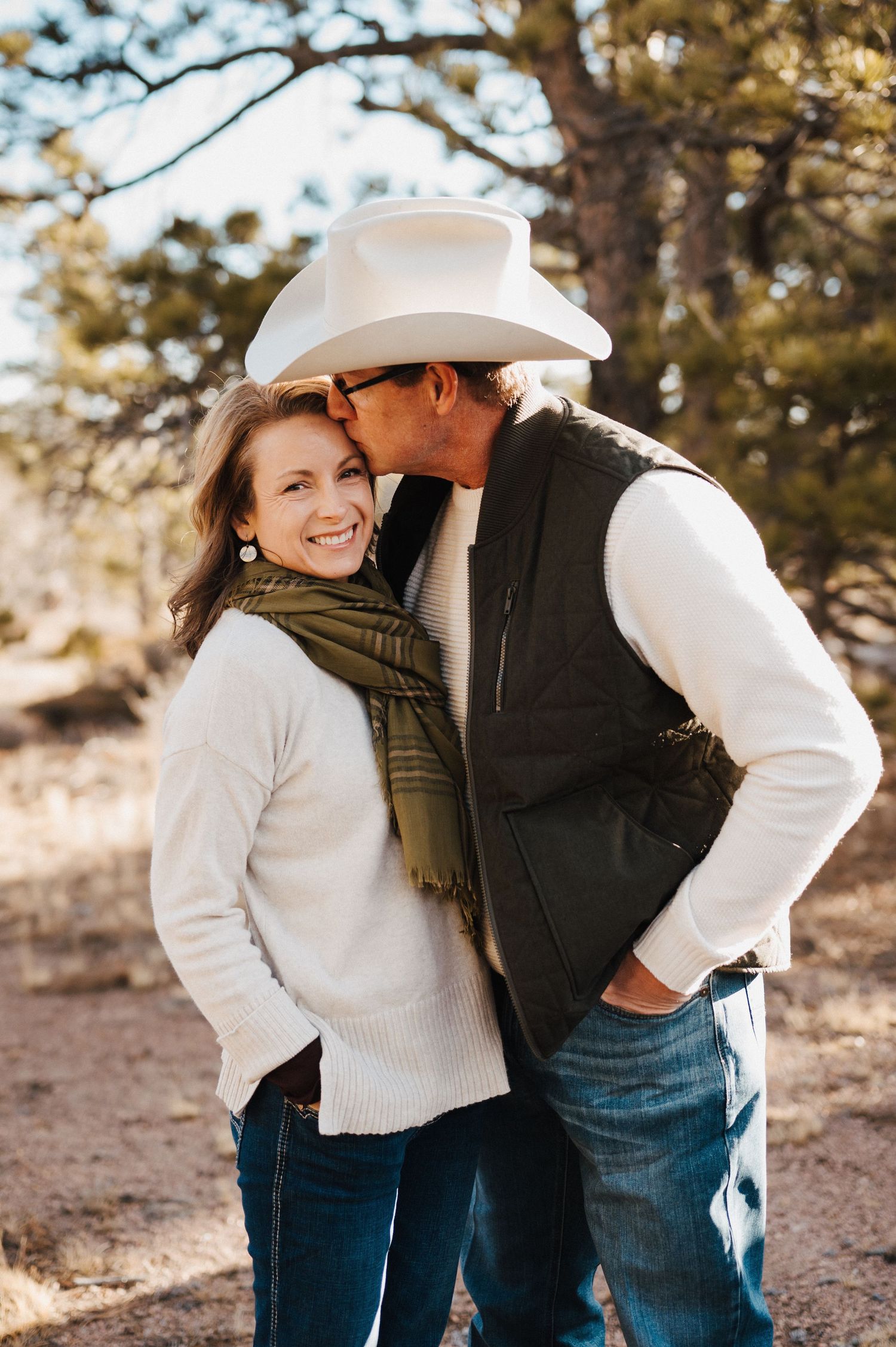 A couple in casual winter attire share intimate moments outdoors against a natural wooded backdrop.