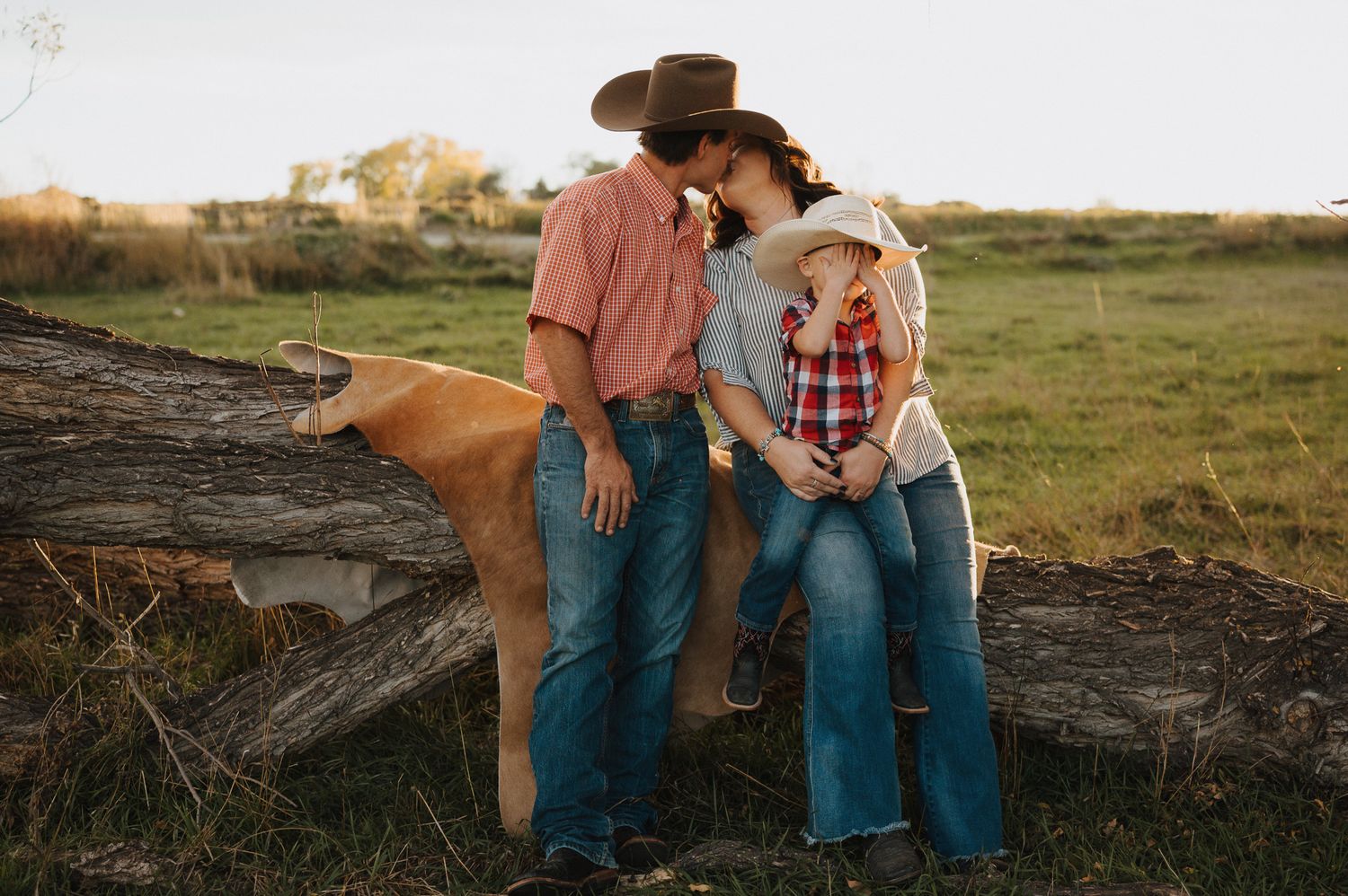 Couple sits on rustic wooden log at sunset in countryside meadow with golden light filtering through.