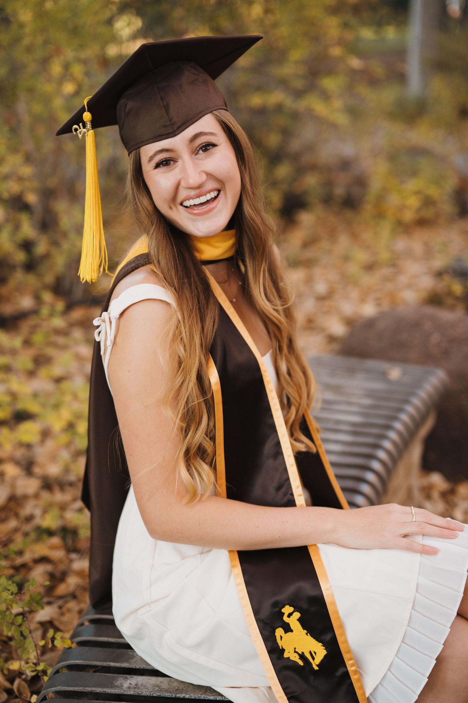 A woman in graduation regalia sitting on a bench in Laramie, Wyoming and smiling.