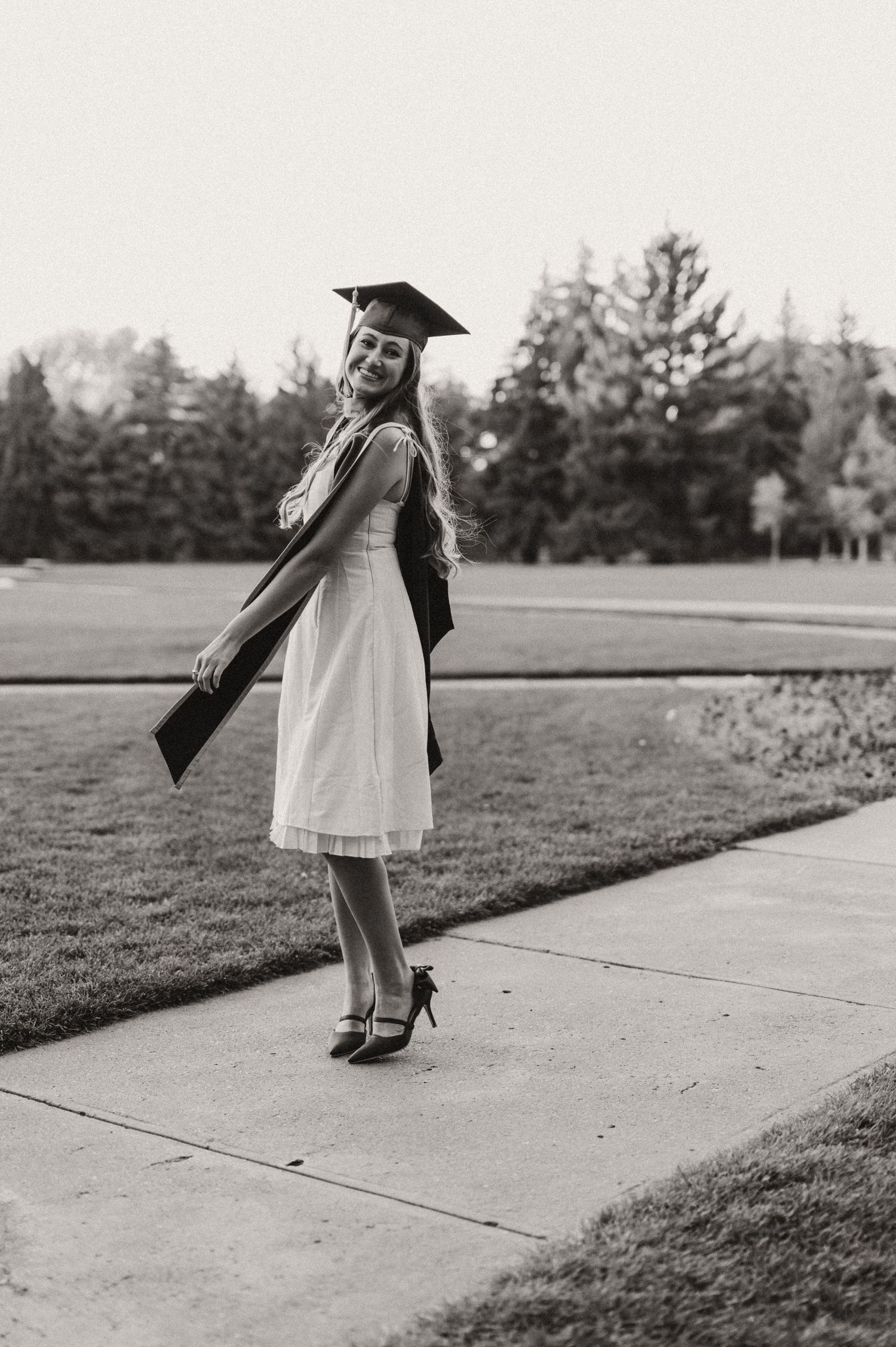 A woman in graduation regalia spinning on a side walk at the University of Wyoming.